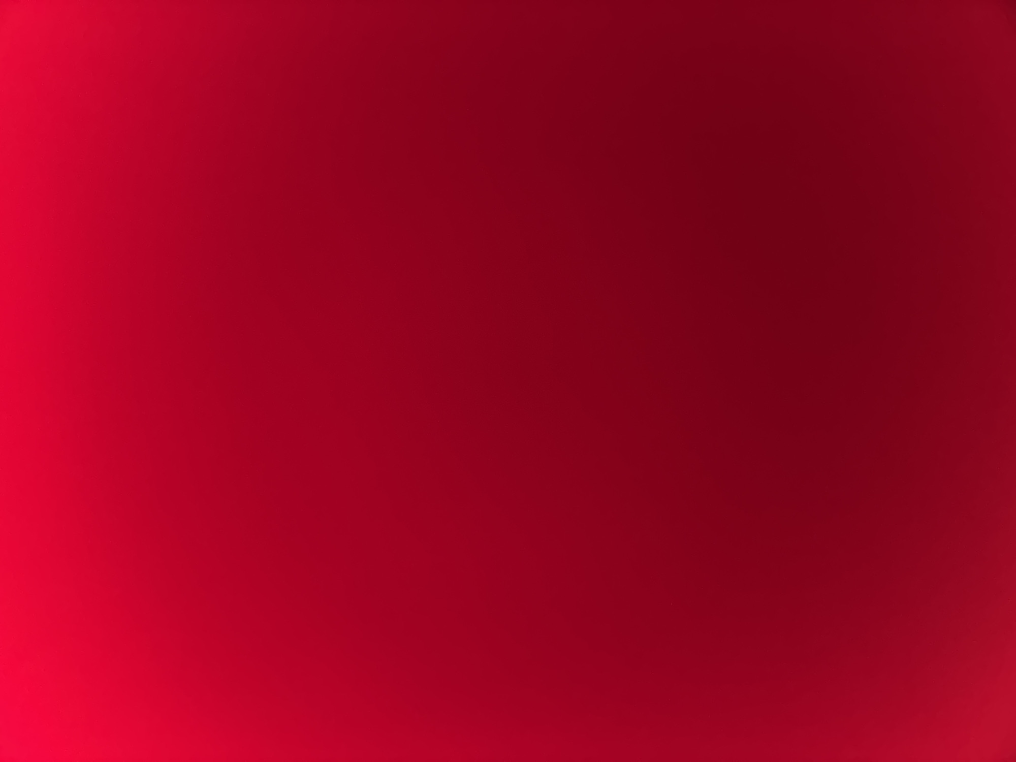 The image presents a solid field of red. A subtle gradient is visible, transitioning from a slightly brighter, lighter red in the upper left quadrant to a deeper, darker crimson in the lower right and bottom edges. The surface appears uniform and smooth, exhibiting no discernible patterns, textures, or imperfections. There are no visible people, subjects, objects, or specific actions depicted within the frame. The environment is entirely abstract, providing no contextual elements or specific landmarks that would allow for the identification of a location within the city of Sofia, Bulgaria. The image exclusively features a continuous, graduating red hue.