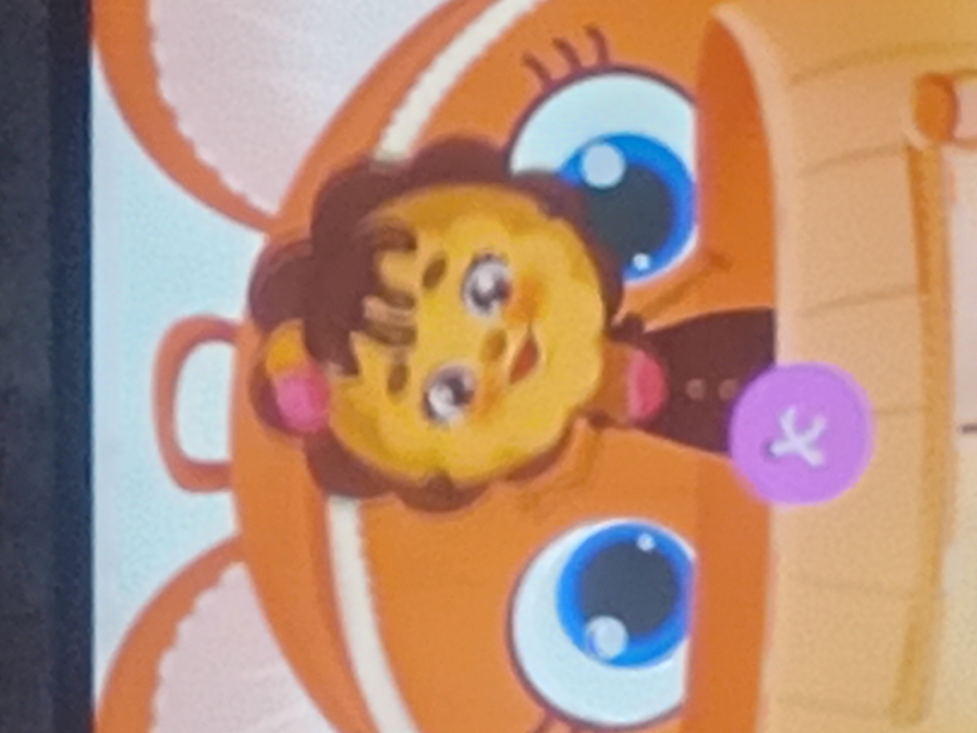 The image is a close-up of a cartoon character, appearing to be a stylized lion cub. The character has a round, yellow face with large, round blue eyes that have white pupils and highlights. It has a brown, fuzzy mane and two small, pinkish circles on its cheeks. The cub is wearing a dark brown garment with a small, light purple button that has a white "x" stitched onto it. The cub's body and ears are a vibrant orange color, with white accents. Behind the cub, a blurred background suggests a light-colored surface, possibly a wall or fabric, with some indistinct orange elements. The overall style is playful and child-like, with bright colors and simplified shapes. There is no discernible time of day, weather, or specific location cues within the image itself, and no visible text. The setting appears to be a digital illustration, possibly from a game or animated program. The cub's expression is cheerful and inviting.