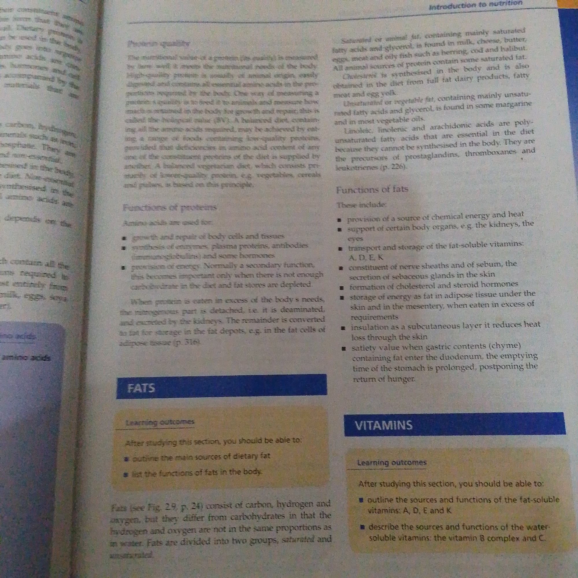 The image is a close-up photograph of two pages from an open textbook, displaying information about nutrition. The left page focuses on "Protein quality" and "Functions of proteins," while the right page discusses "Introduction to nutrition," "Functions of fats," and sections titled "FATS" and "VITAMINS" with associated "Learning outcomes." The text is primarily in English. The lighting suggests an indoor setting, possibly under artificial light or near a window. There is no indication or visible element within the image that would suggest a location in Jalingo, Nigeria.