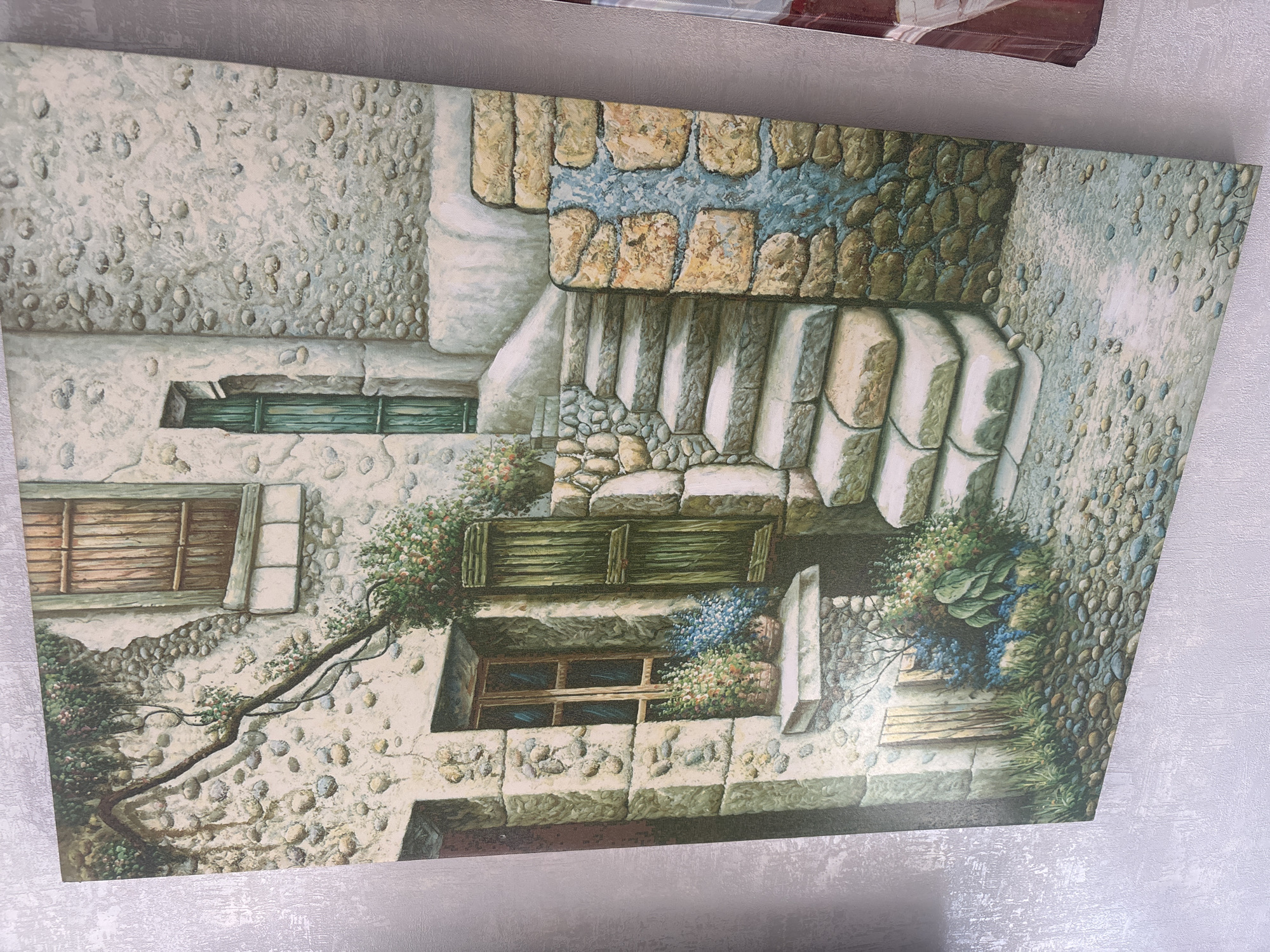 The image is a close-up of a painting depicting a rustic stone courtyard with a set of stairs. The painting features a stone wall with a wooden shuttered window, a green wooden door, and stone steps leading upwards. There are also potted plants and flowers adding color to the scene. The ground is covered with cobblestones. The painting style is realistic, with attention to detail in the textures of the stone and wood. There are no people or animals visible in the painting.
This image does not show any specific location in the city of Krasnodar, Russia. The scene depicted is a generic representation of a European-style courtyard, likely inspired by Mediterranean or southern European architecture. There are no discernible landmarks, signs, or architectural elements that would identify it as being from Krasnodar.