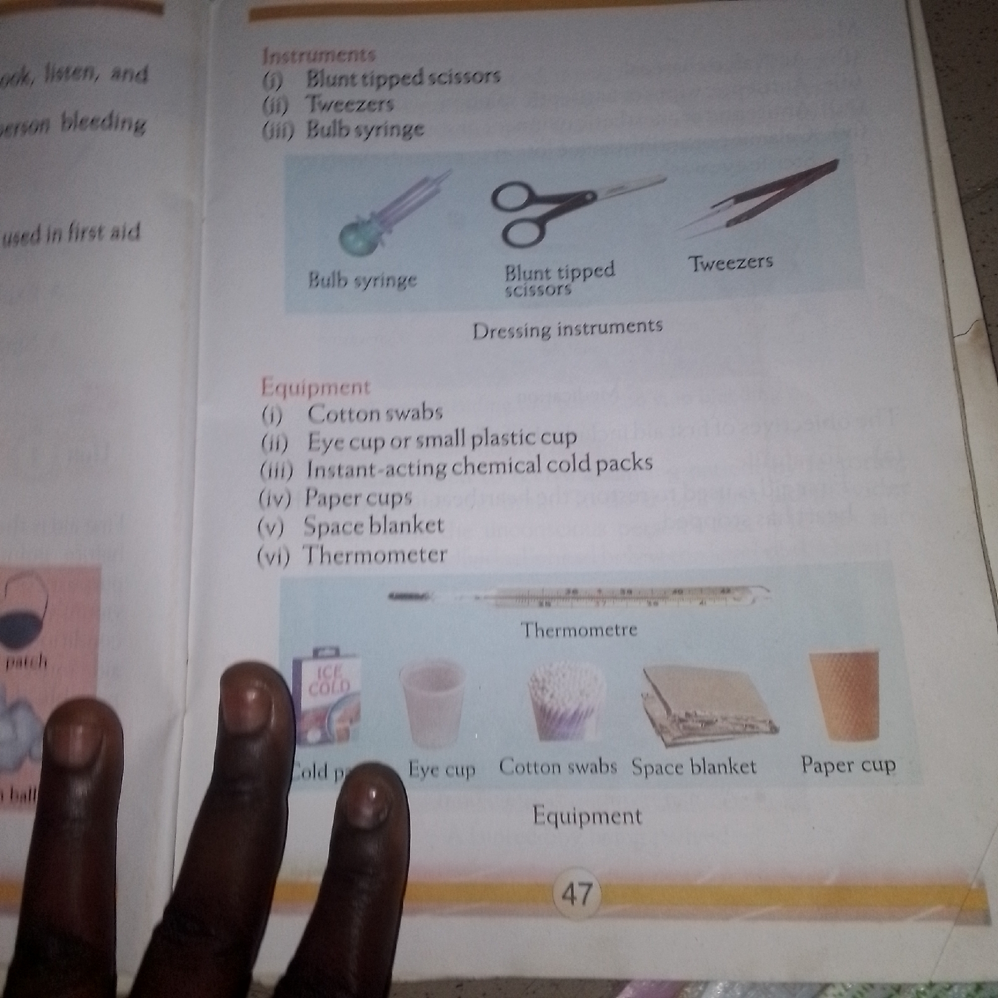 The image is a photograph of an open book, likely a textbook, displaying information about first aid. On the left side of the page, there is text related to first aid procedures and equipment, partially obscured by fingers. The right side of the page is dominated by illustrations and text describing various first aid instruments and equipment.
Specifically, the top section of the right page lists "Instruments" with three items: (i) Blunt tipped scissors, (ii) Tweezers, and (iii) Bulb syringe. Below this, there are illustrations of these three items. The bulb syringe is depicted on the left, followed by blunt tipped scissors in the middle, and tweezers on the right. Beneath these illustrations, the text "Dressing instruments" is present.
The lower section of the right page is dedicated to "Equipment". A numbered list includes: (i) Cotton swabs, (ii) Eye cup or small plastic cup, (iii) Instant-acting chemical cold packs, (iv) Paper cups, (v) Space blanket, and (vi) Thermometer. This list is accompanied by a series of images depicting these items. From left to right, the images show a box labeled "ICE COLD", an eye cup, cotton swabs, a space blanket, and a paper cup. A thermometer is also illustrated above these items, with text indicating "Thermometer".
The bottom edge of the page shows a page number "47" within a circular emblem. The overall presentation suggests an educational context, likely for teaching first aid. There is no information in the image that provides any details about the location in the city of Unknown, Unknown.