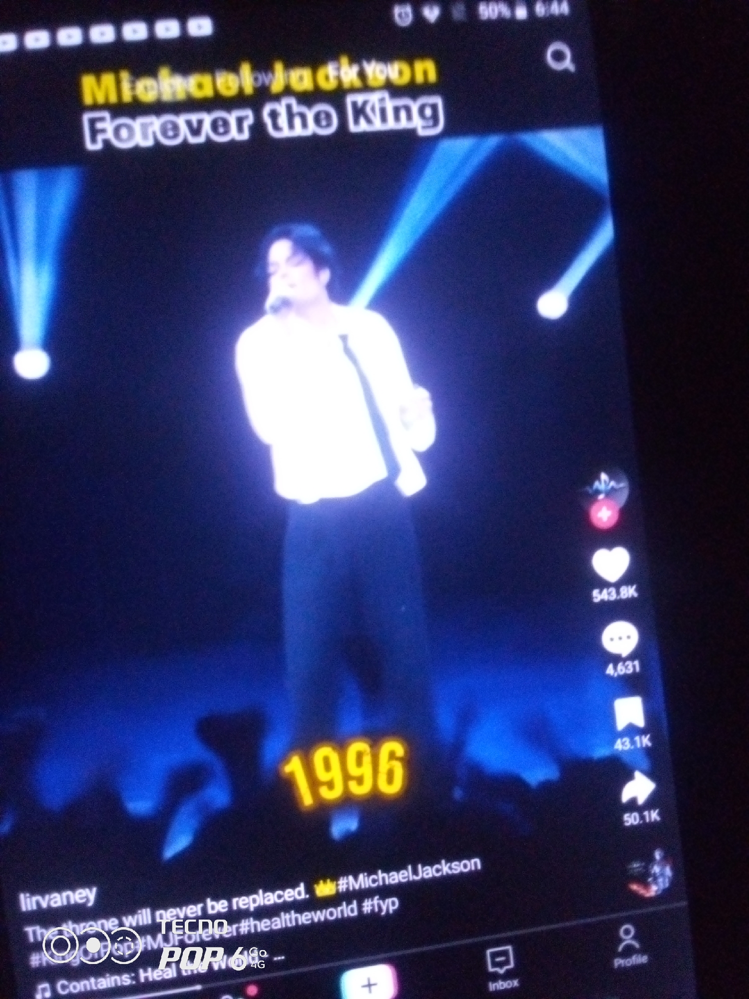 The image is a screenshot of a TikTok video featuring Michael Jackson. The video displays the text "Michael Jackson Forever the King" in large font, with "1996" also prominently displayed. Michael Jackson is seen in silhouette, wearing a white shirt and dark pants, performing on a stage with blue spotlights. The bottom of the screen shows typical TikTok interface elements like likes, comments, shares, and profile icons, along with text that reads "lirvaney," "The throne will never be replaced. #MichaelJackson," and "Contains: Heal the World." The location of Howayi, Nigeria is not mentioned or discernible from the image.
