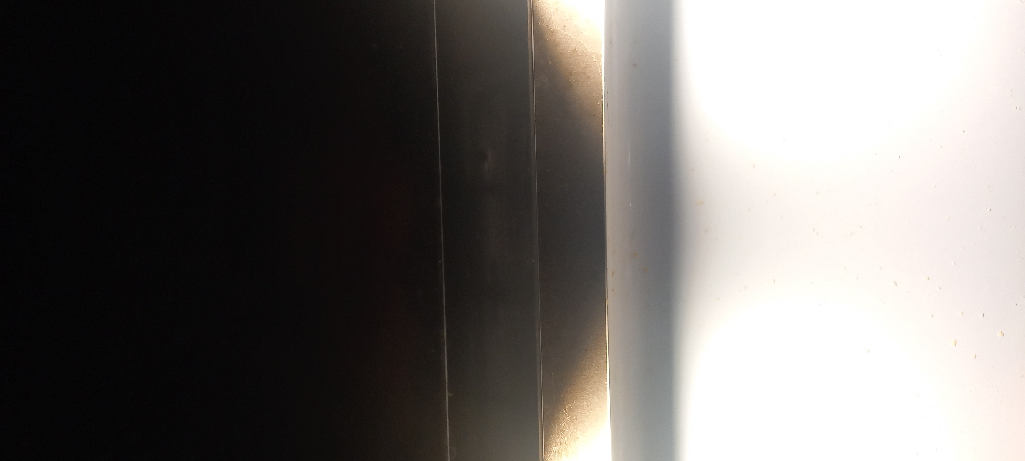 The image depicts a close-up of a dark, likely black, surface on the left transitioning to lighter, possibly metallic surfaces in the middle, and finally to a bright white surface on the right. The surfaces appear to be vertical panels or structures placed next to each other. The overall impression is that it is an indoor setting with artificial lighting. There is no indication of location in the city of Kryvyi Rih, Ukraine, people, subjects, actions, interactions, or the environment.
