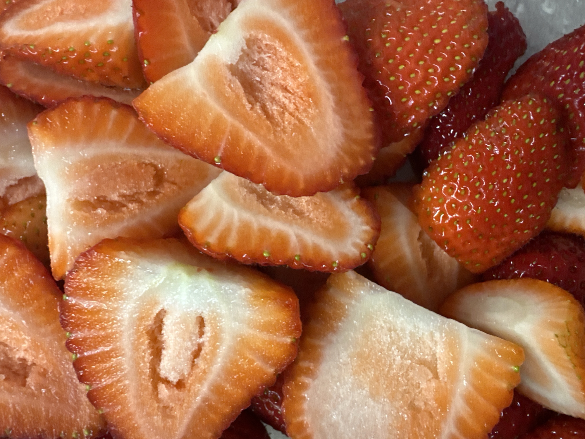 The image shows a close-up view of sliced strawberries. Some strawberries are sliced, revealing their pale interior, while others are whole. The strawberries are a bright red color with visible seeds on their surface. The scene appears to be indoors under artificial lighting. The location in Sofia, Bulgaria, is not evident from the image content.