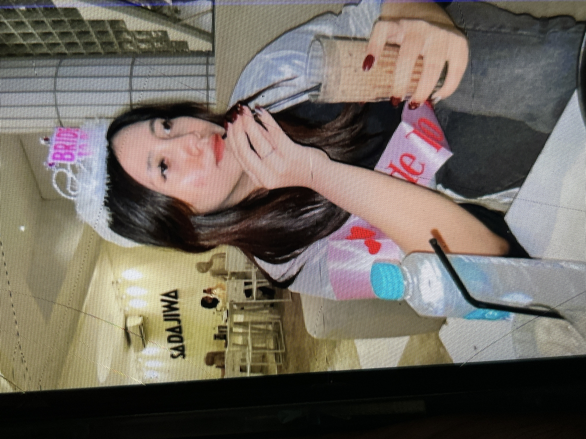 The image, likely taken in Depok, Indonesia, depicts a young woman wearing a "Bride" tiara and sash, suggesting a bachelorette party. She is seated in what appears to be a cafe or restaurant, with the "SADAJIWA" logo visible in the background, indicating the establishment's name. The woman holds a drink in her right hand and touches her lips with her left hand. A bottle of water with a straw is positioned in front of her. The environment appears casual, with other patrons and tables visible in the background. The lighting suggests an indoor setting, possibly during the day or evening.