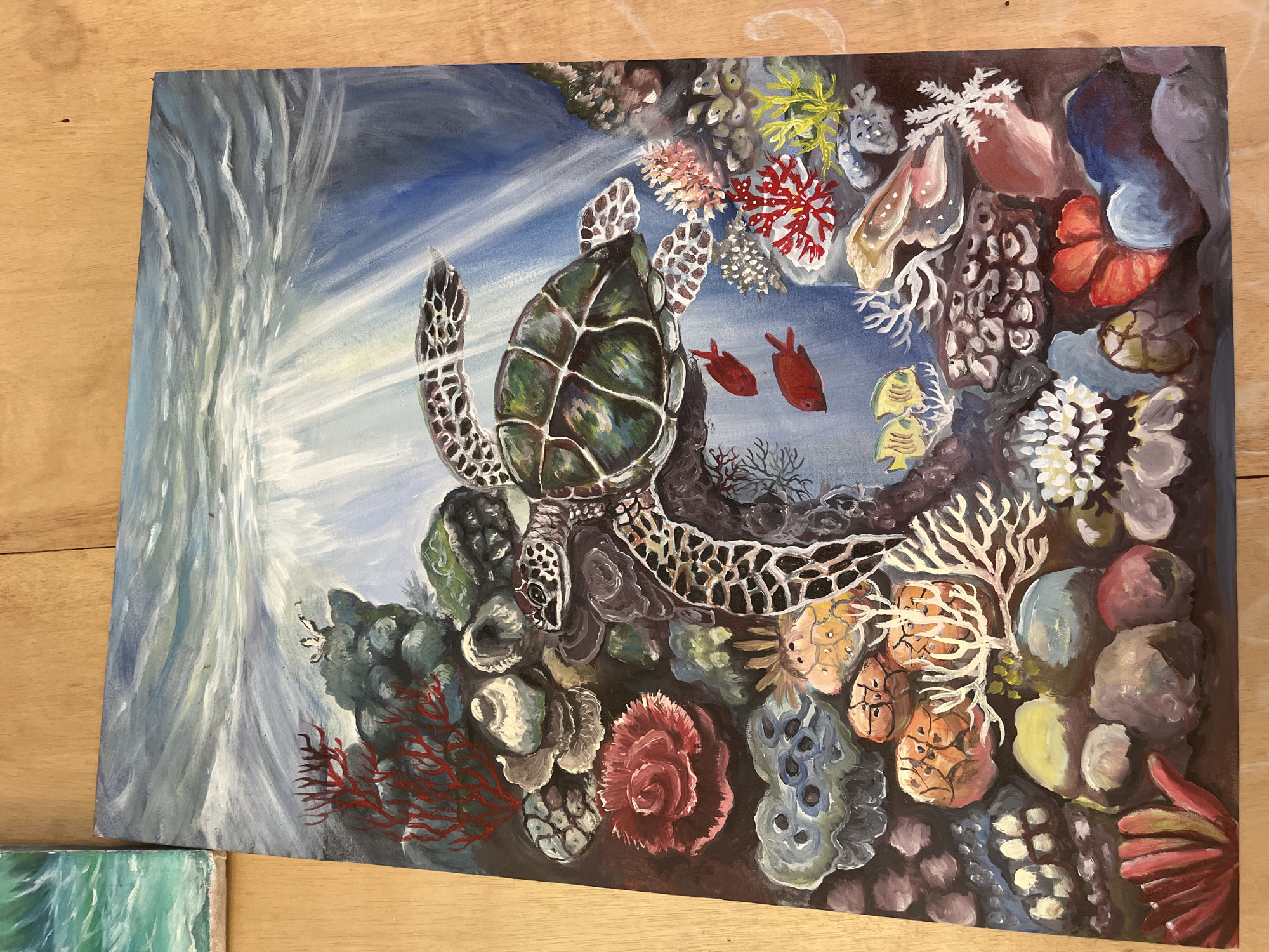 A painting depicts a sea turtle swimming among colorful coral reefs. Two red fish swim near the turtle, and sun rays stream down from the surface of the water on the left side of the image. There is no city or location mentioned or depicted in the image.