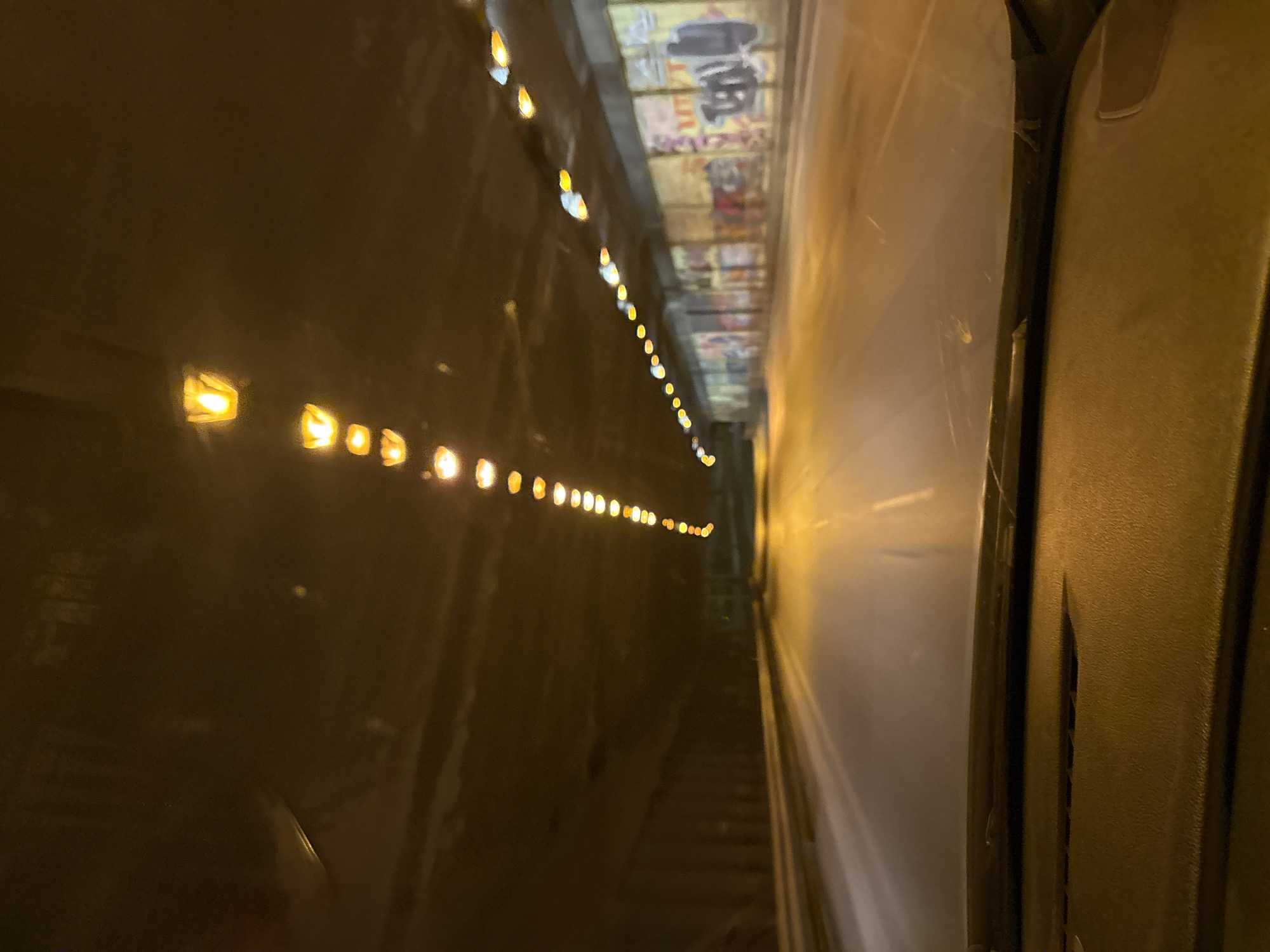 The image shows the inside of a tunnel in Sofia, Bulgaria. A line of lights is visible along the side wall of the tunnel, stretching into the distance. The tunnel ceiling appears to have posters or panels. The right side of the frame is taken up by the interior of a vehicle.