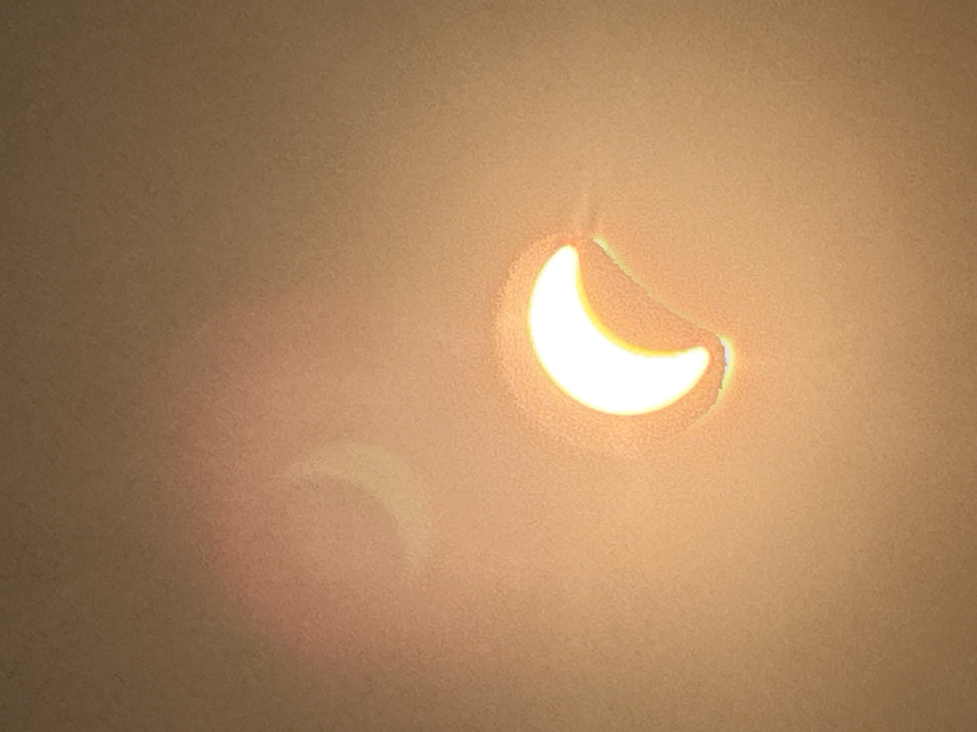 The image depicts a partial solar eclipse as viewed through what appears to be a projection onto a surface. Two crescent shapes of light are visible, with the brighter and more defined one in the lower right quadrant and a fainter, more diffuse one in the upper left quadrant. The background is a mottled, uniform brown or beige surface. There are no people, objects, or discernible environmental features within the image that would suggest a specific location in Märstetten, Switzerland. The image captures a celestial event, not a terrestrial scene.