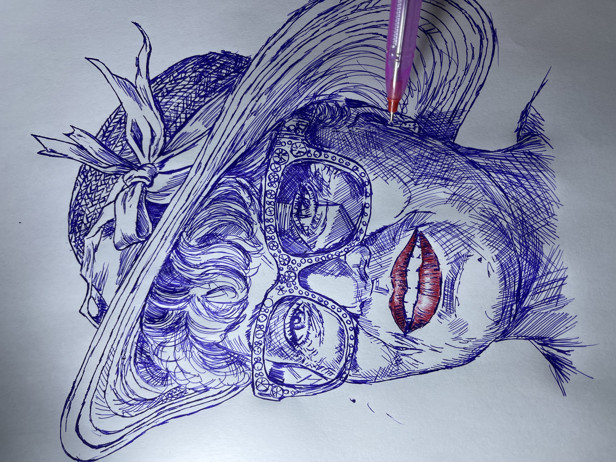 A pen-and-ink drawing depicts a woman's face, wearing a wide-brimmed hat and large, decorative eyeglasses. The drawing is rendered in blue ink with cross-hatching for shading and detail, except for the lips, which are colored in red. A pink pen is shown partially in the lower right corner, appearing to be in the process of drawing or having just completed a section. The background is a plain, off-white surface. There is no information in the image that relates to the city of Jos, Nigeria.