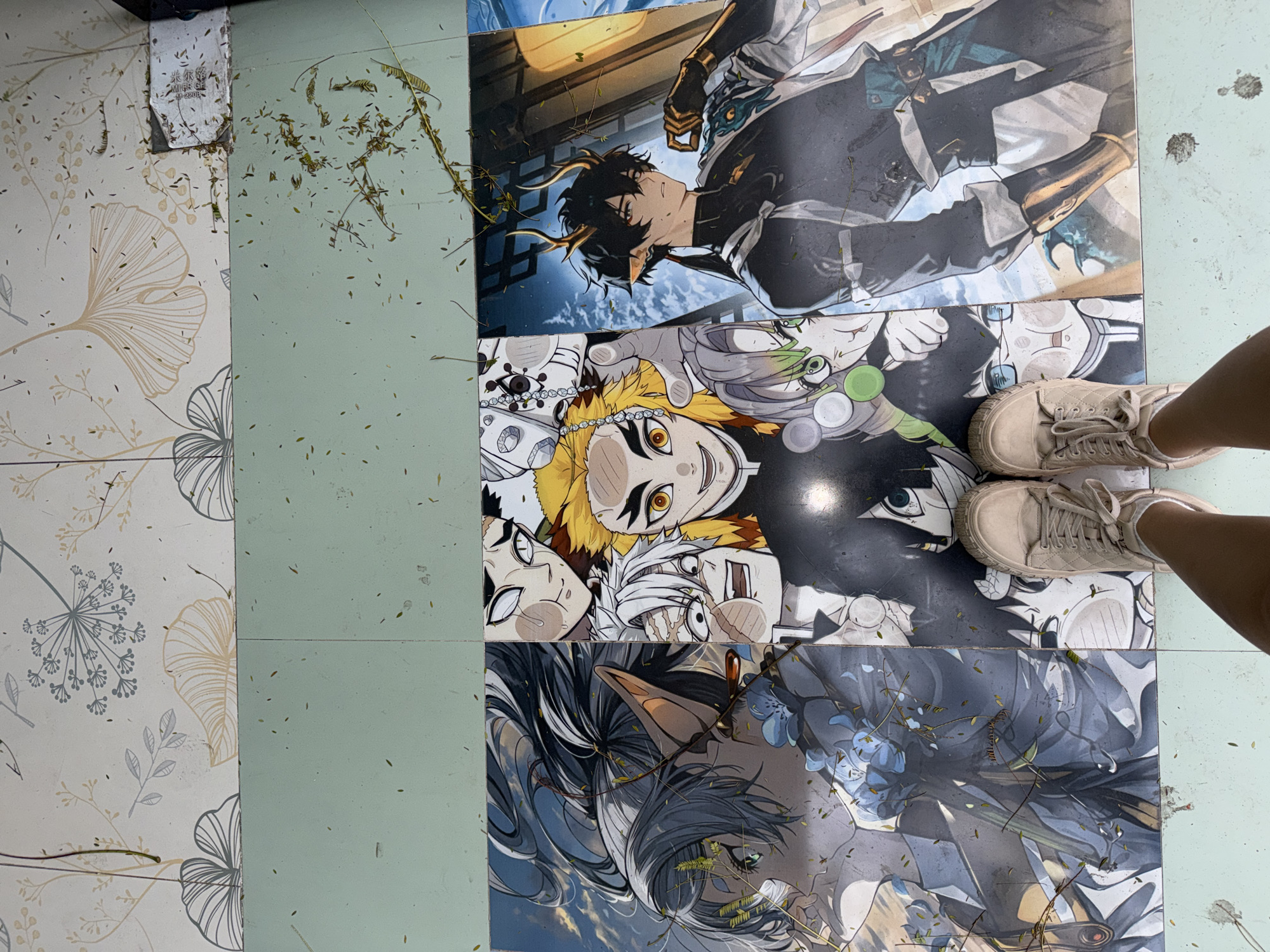 The image depicts a floor made of tiles, partially covered in dried leaves and debris. Some of the tiles are patterned with floral designs, while others are plain light green. Three tiles display anime-style character illustrations. A pair of beige sneakers and a portion of a person's legs are visible in the top-right corner. The location is Chongqing High-tech Zone, China.
