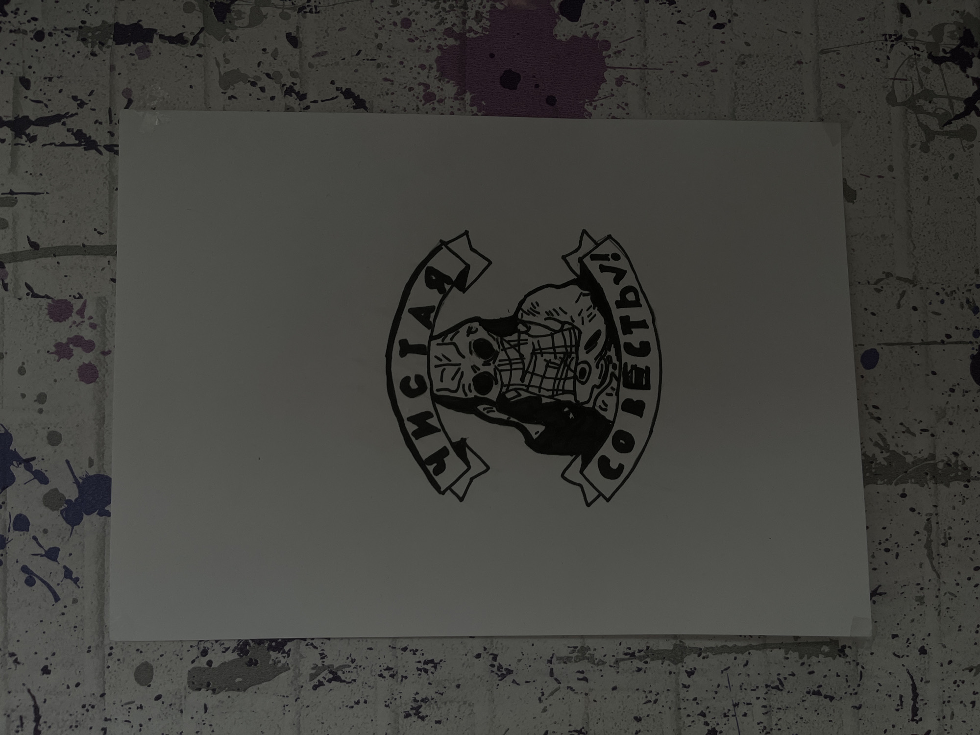A black-and-white graphic image is affixed to a wall. The wall has a white base with splatters of paint in various colors, including black, purple, and gray.
The graphic is centered on a rectangular sheet of paper. The image depicts a skull or face covered by a hockey mask, with the words "Чистай Совесть!" (Clean Conscience!) curving around it, printed on a banner-like design. The style is reminiscent of a stencil or block print.
The image does not depict a specific location in Maladzyechna, Belarus.