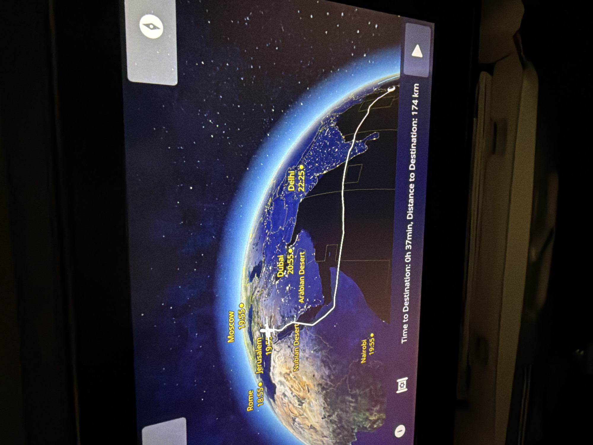 The image shows an in-flight entertainment screen displaying a flight map. The map depicts a view of Earth from space, highlighting areas including Rome, Jerusalem, Moscow, Dubai, Delhi, and Nairobi. The plane's current location appears to be near Jerusalem. The screen indicates that the remaining flight time is 0 hours and 37 minutes, with a distance to the destination of 174 kilometers.