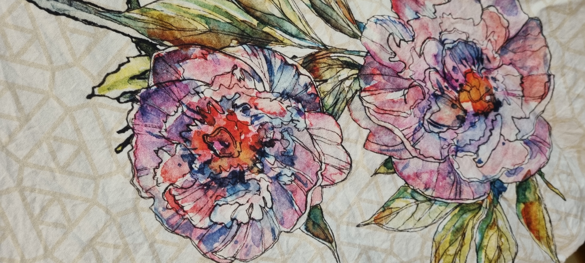 The media file is a close-up, overhead shot of a fabric pattern featuring watercolor-style illustrations of flowers and geometric shapes. The subjects are two large, stylized flowers, likely peonies, with intricate petal formations. The flowers are rendered in a vibrant color palette of pinks, purples, blues, and reds, with black outlines defining their shapes. Interspersed among the flowers are green leaves, also depicted in a watercolor style with visible brushstrokes and color variations.
Beneath and behind the floral elements, a subtle geometric pattern of intersecting lines forms a light tan grid. This pattern appears to be printed onto the fabric, providing a textured background that contrasts with the fluid watercolor artwork. The fabric itself has a slightly crinkled or textured appearance, suggesting it could be linen or a similar natural fiber.
There is no activity or event taking place, as the image is a static depiction of a decorative pattern. There are no people visible. The lighting is even, indicating an indoor setting or diffused daylight, with no strong shadows. No time of day, weather, or specific location cues are apparent within the image itself, other than the general context of "Romashkovo, Russia" provided. The overall mood conveyed is artistic and decorative, with the vibrant colors and floral subject matter suggesting a sense of natural beauty and perhaps a touch of elegance. There is no visible text in the image.