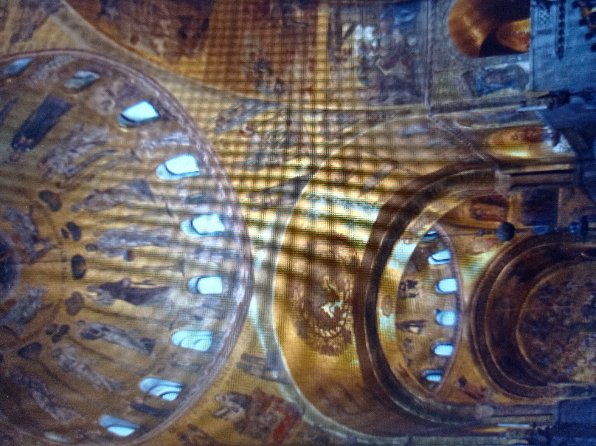 The image shows the interior of a grand, ornate building with golden domes and arches, decorated with intricate mosaics. The mosaics depict numerous figures, likely religious or historical, in various poses and scenes. Arched windows with bright blue light are visible along the upper sections of the domes. The overall impression is one of opulent architecture and detailed artwork. The location is the St. Mark's Basilica in Venice, Italy, not Mukachevo, Ukraine.
