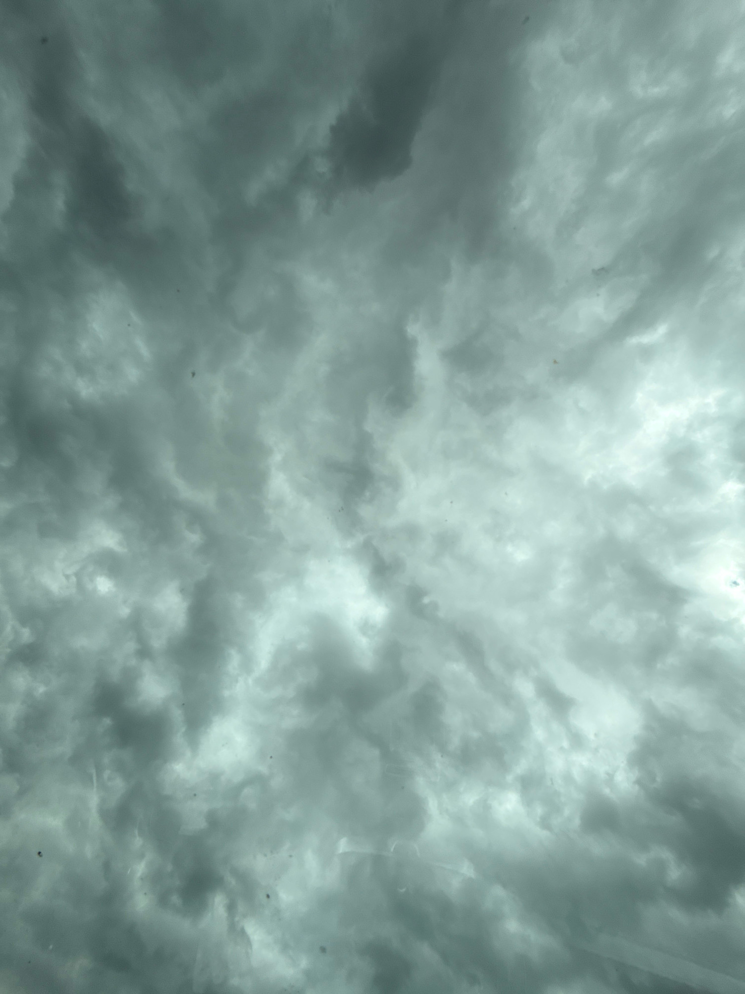 The image is a photograph of a stormy sky, viewed from below. Dark, heavy clouds dominate the frame, with patches of lighter grey and white indicating breaks or thinner areas in the cloud cover. The overall impression is one of an overcast day with impending rain. There are no discernible landmarks or urban features visible in the image, making it impossible to determine a specific location within the city of Werther, Germany. The scene is devoid of any people, subjects, objects, or actions. The environment depicted is solely the sky and clouds.