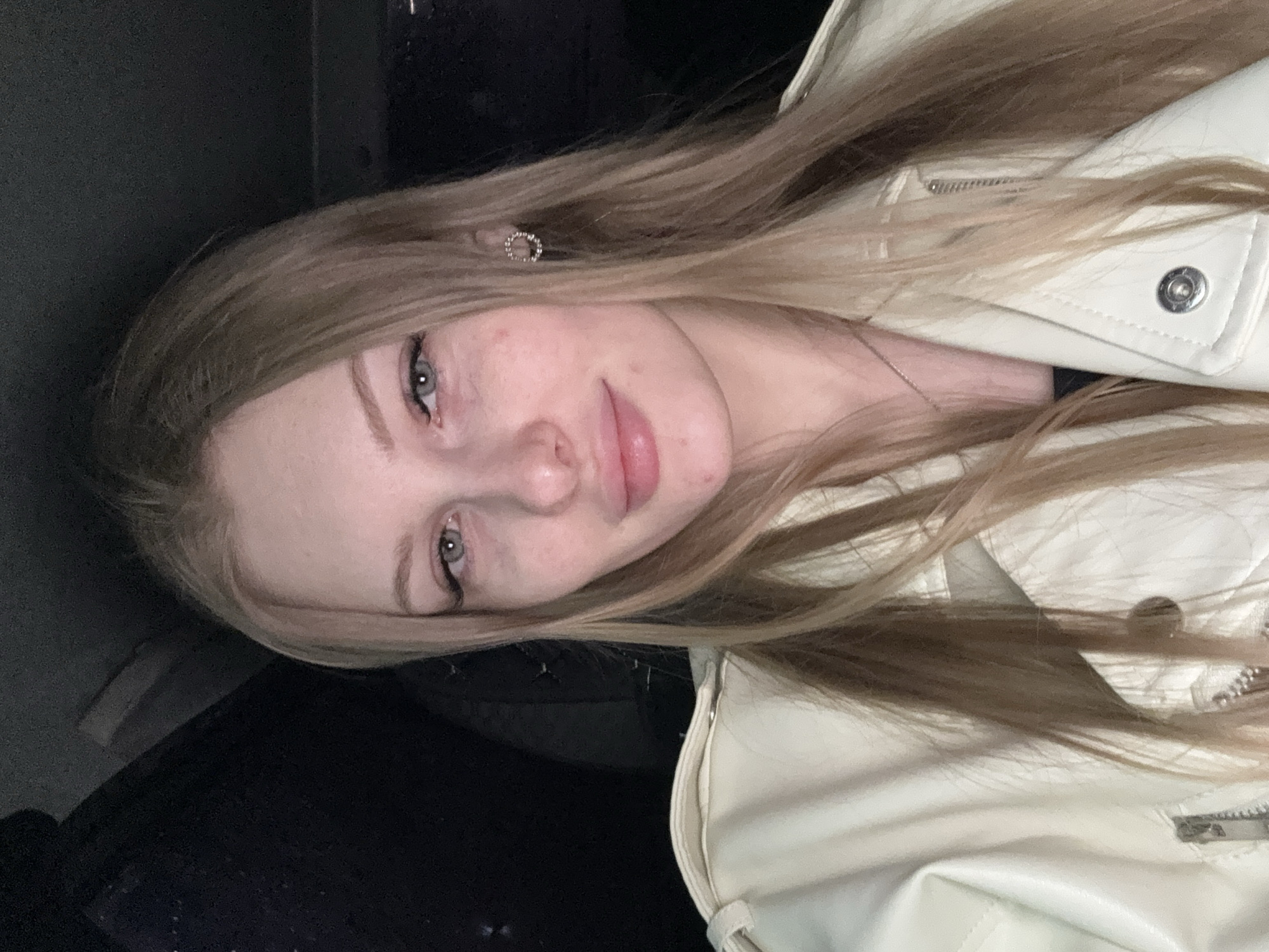 A young woman with long, light brown hair is facing the camera. She has fair skin, light eyes, and is wearing a light-colored jacket. She has an earring in her left ear. The background is dark, suggesting an indoor or nighttime setting. The location, Perm, Russia, is not discernible from the visual information provided.