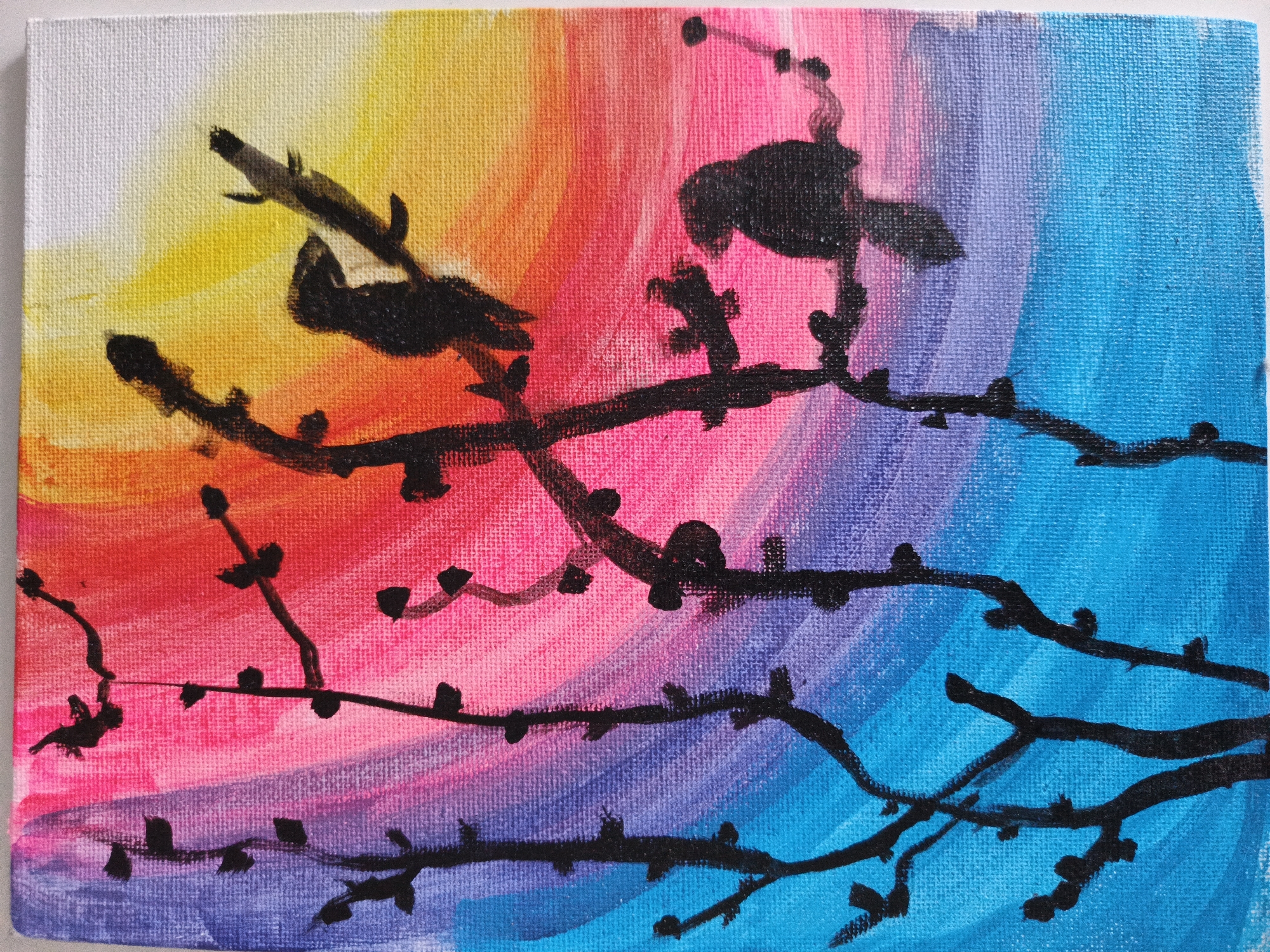 This image is a detailed photograph of an acrylic or oil painting on a textured canvas. The artwork depicts a stylized outdoor scene, likely a sunset or sunrise, characterized by a vibrant gradient sky and silhouetted foreground elements. The background features a sweeping color transition: white and pale yellow in the upper left, progressing through bright yellow, orange, and fuchsia pink across the central portion, then into shades of lavender, deep purple, and vivid blue towards the right and bottom right. Distinct brushstrokes are visible, indicating the direction of paint application, and the weave of the canvas material is clearly evident throughout. Superimposed against this colorful backdrop are several solid black silhouettes of barren tree branches, featuring small, rounded buds or nascent leaves. These branches extend horizontally and diagonally across the lower two-thirds of the canvas. Two prominent black bird silhouettes are positioned in the upper half of the painting; one is situated on a branch in the upper left, and another is perched on a branch in the upper right. The painting is an artistic rendition and does not depict a real-world location in the city of Unknown, Unknown.