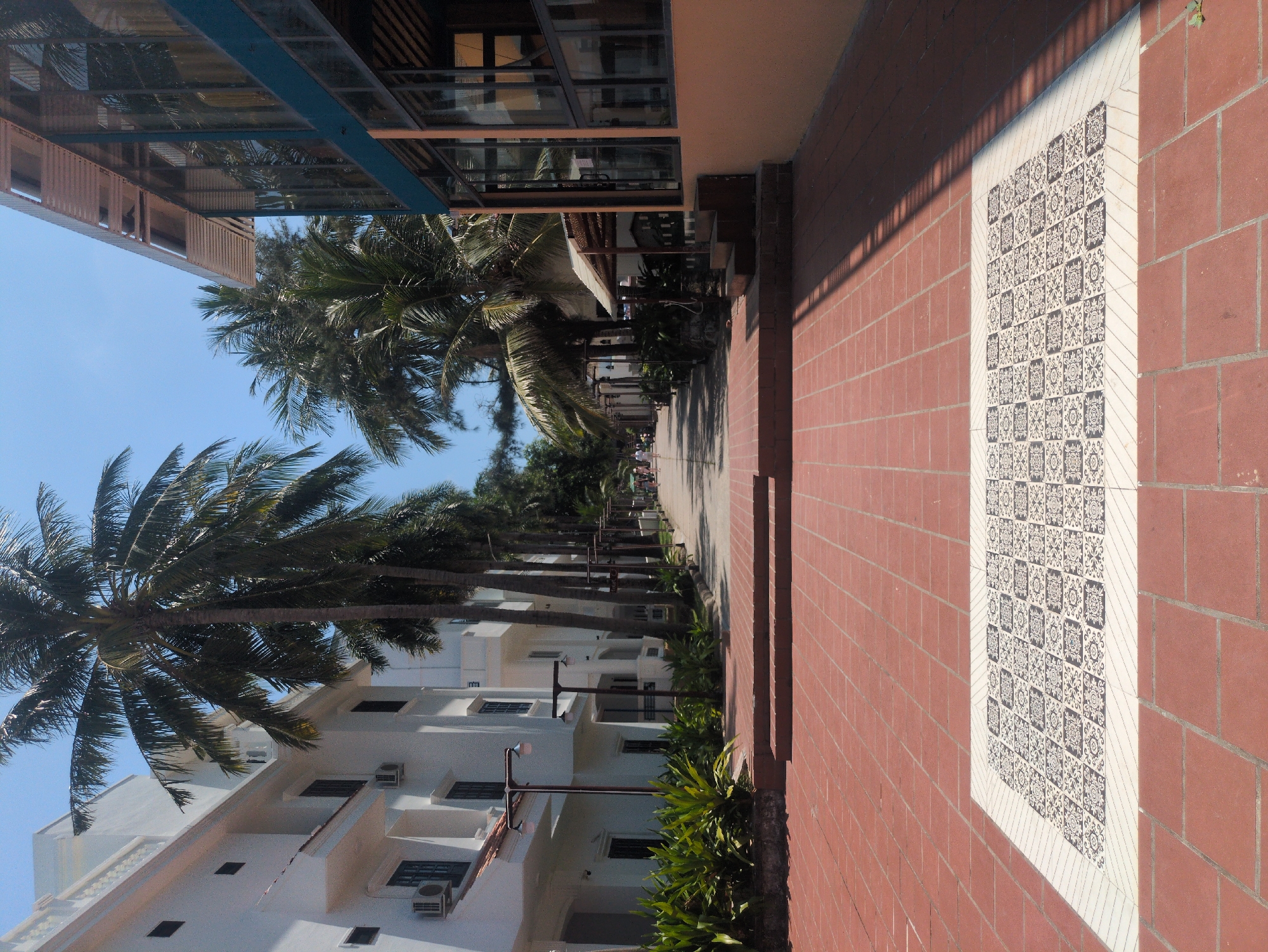A brick sidewalk leads into the distance in Phú Quốc, Vietnam. Buildings border the sidewalk on both sides. Palm trees line the street.