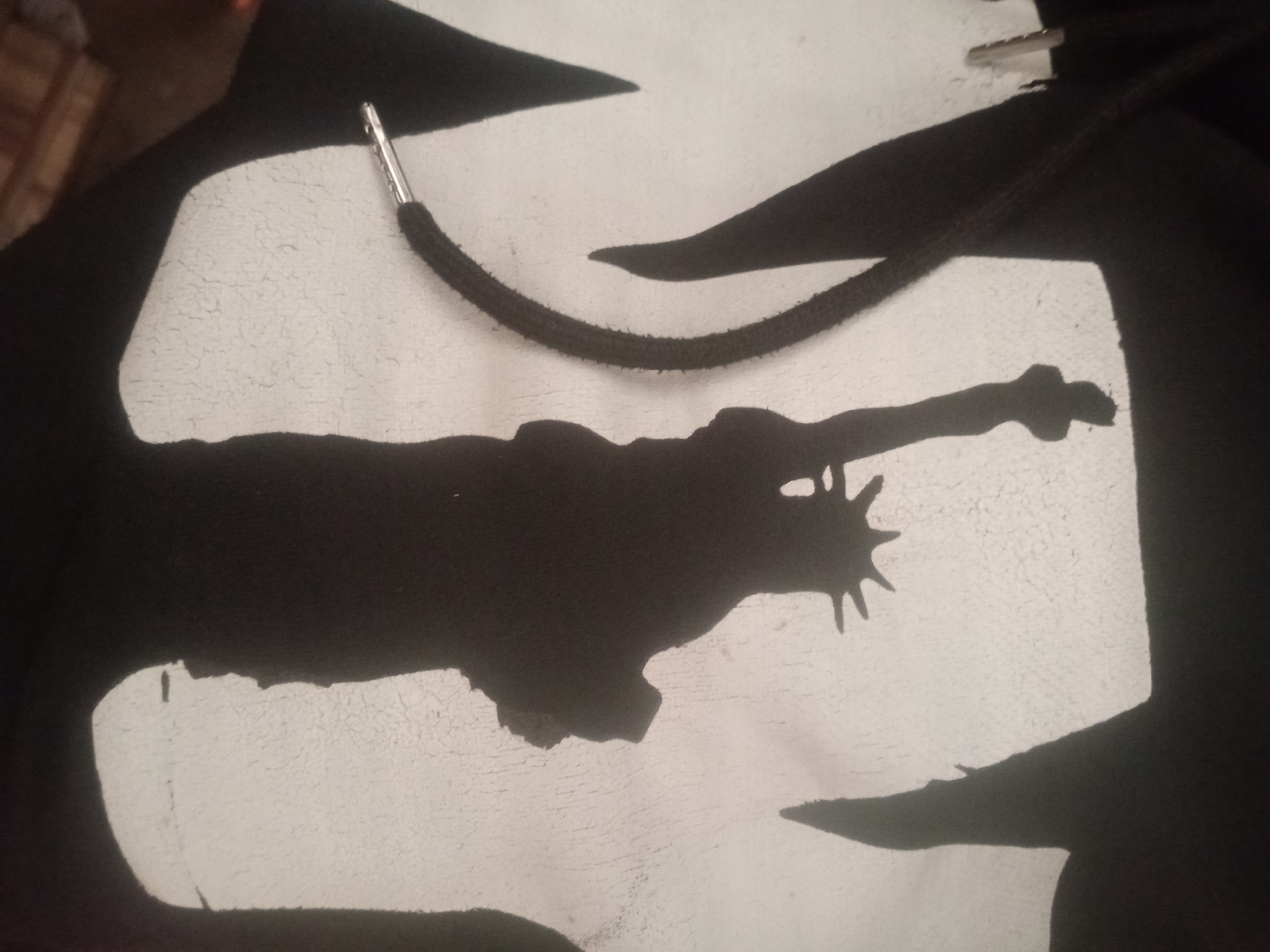 The image shows a close-up view of a black hoodie with a white graphic. The graphic appears to be a silhouette of the Statue of Liberty. The hoodie has a drawstring, and the end of the drawstring is visible in the upper left quadrant of the image. The background of the image is dark and out of focus. There are no people or other identifiable objects in the scene. The location of this image in Jalingo, Nigeria is not discernible from the visual information provided.