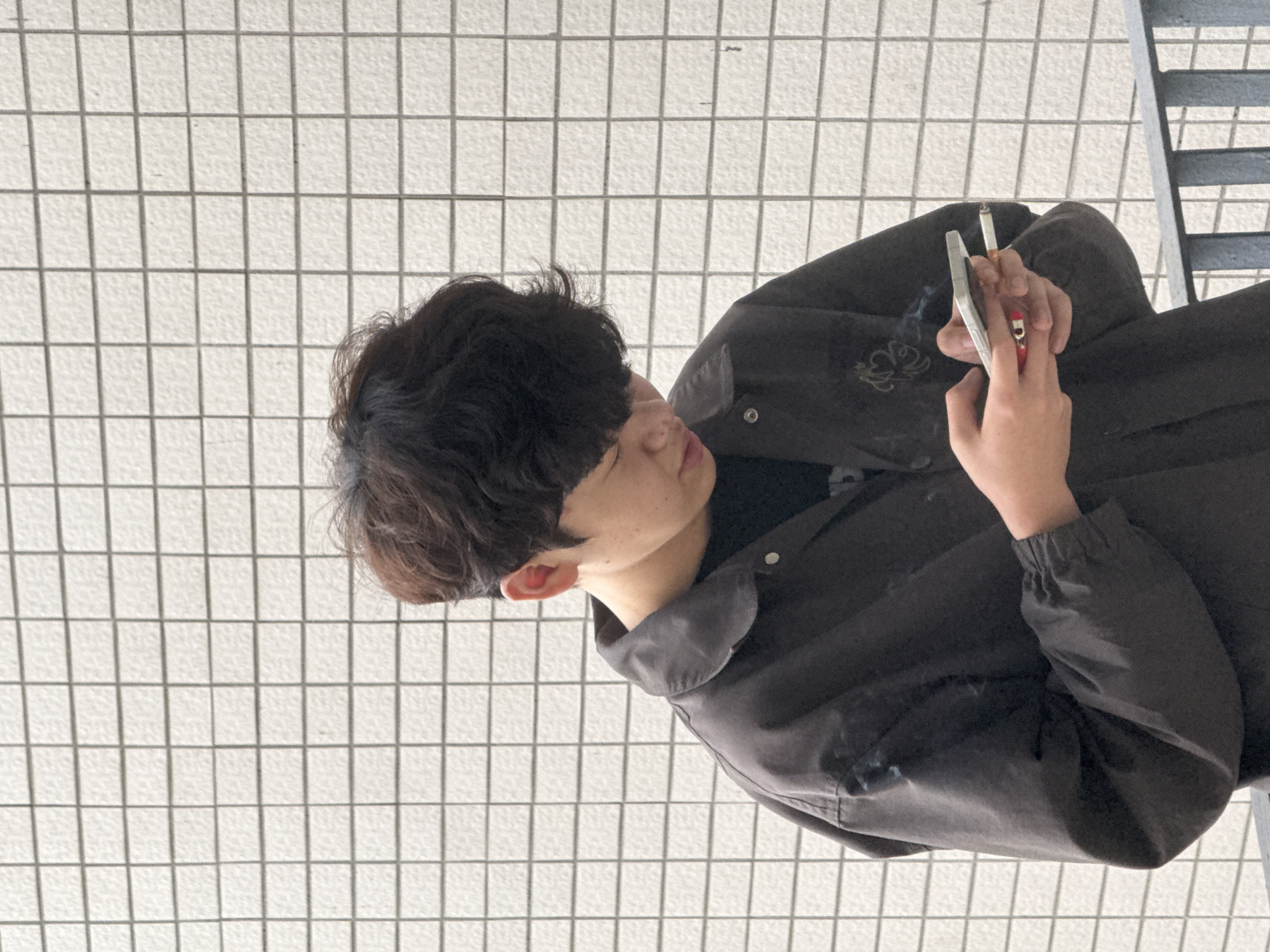 An individual is holding a lit cigarette and a lighter. The person is wearing a dark jacket. The environment is a tiled floor and a set of stairs. There is no information about the specific location in Jiangjin, China.