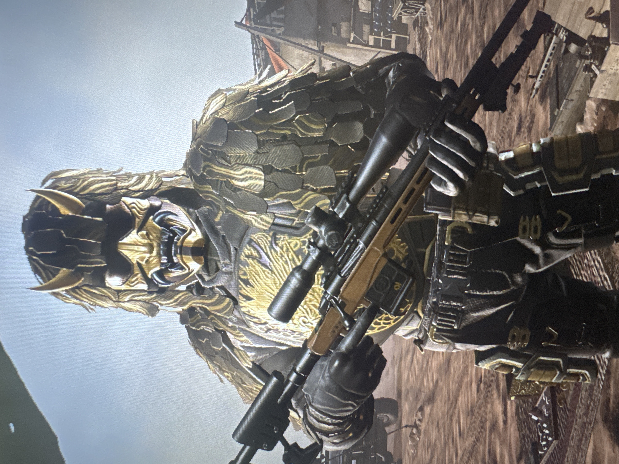 The image shows a close-up of a video game character wearing a gold and black ornate armor set with a mask resembling a Japanese demon or oni. The character is holding a sniper rifle. The background appears to be a desert or arid environment with some structures and a vehicle visible, suggesting a military or combat setting within the game. The scene is a still from a video game, not a real-world location. There is no information that links this image to the city of Stepnogorsk, Kazakhstan.