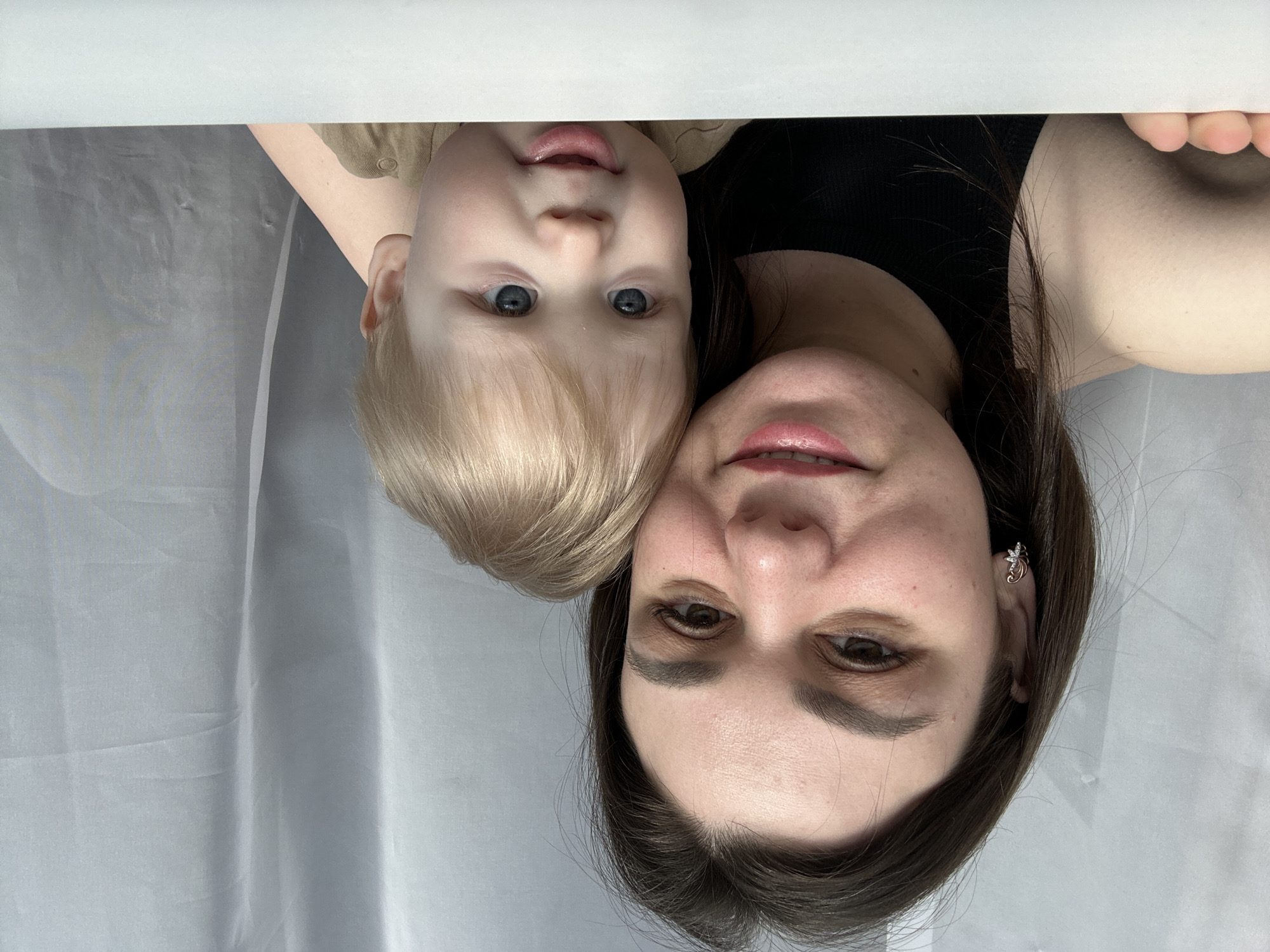 The image shows a woman and a young child, possibly a mother and her son, posing closely together. The child has light blond hair and blue eyes. The woman has brown hair and is wearing a black top. The background appears to be a light-colored wall or curtain. The image is taken in a close-up, head-and-shoulders shot. It is impossible to identify the location as Chaikovsky, Russia, or any specific place based on the image alone.