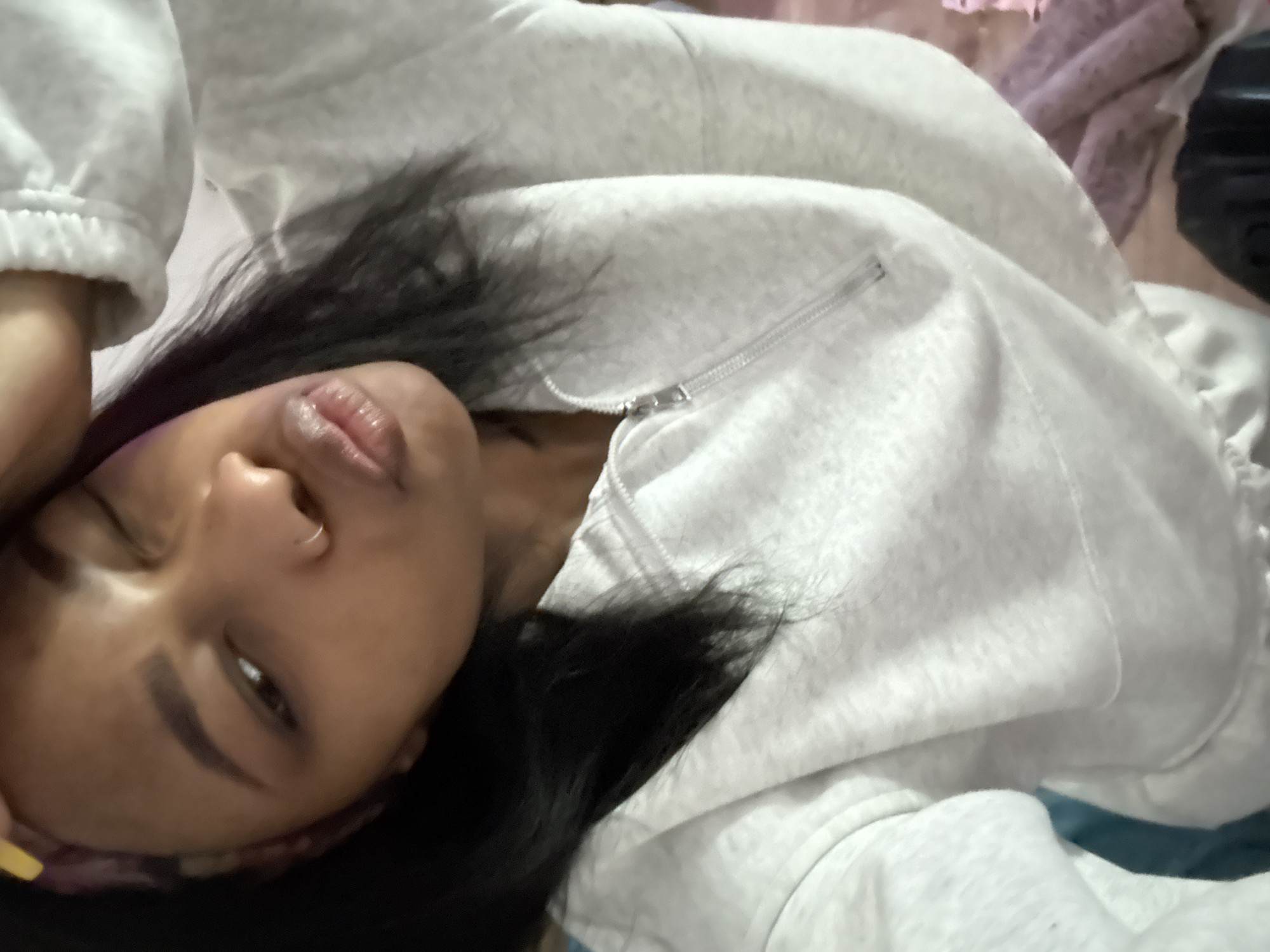 A woman with dark hair and a nose ring is lying down, wearing a light gray zip-up hoodie. The location in the city of Troitsk, Russia is unknown.