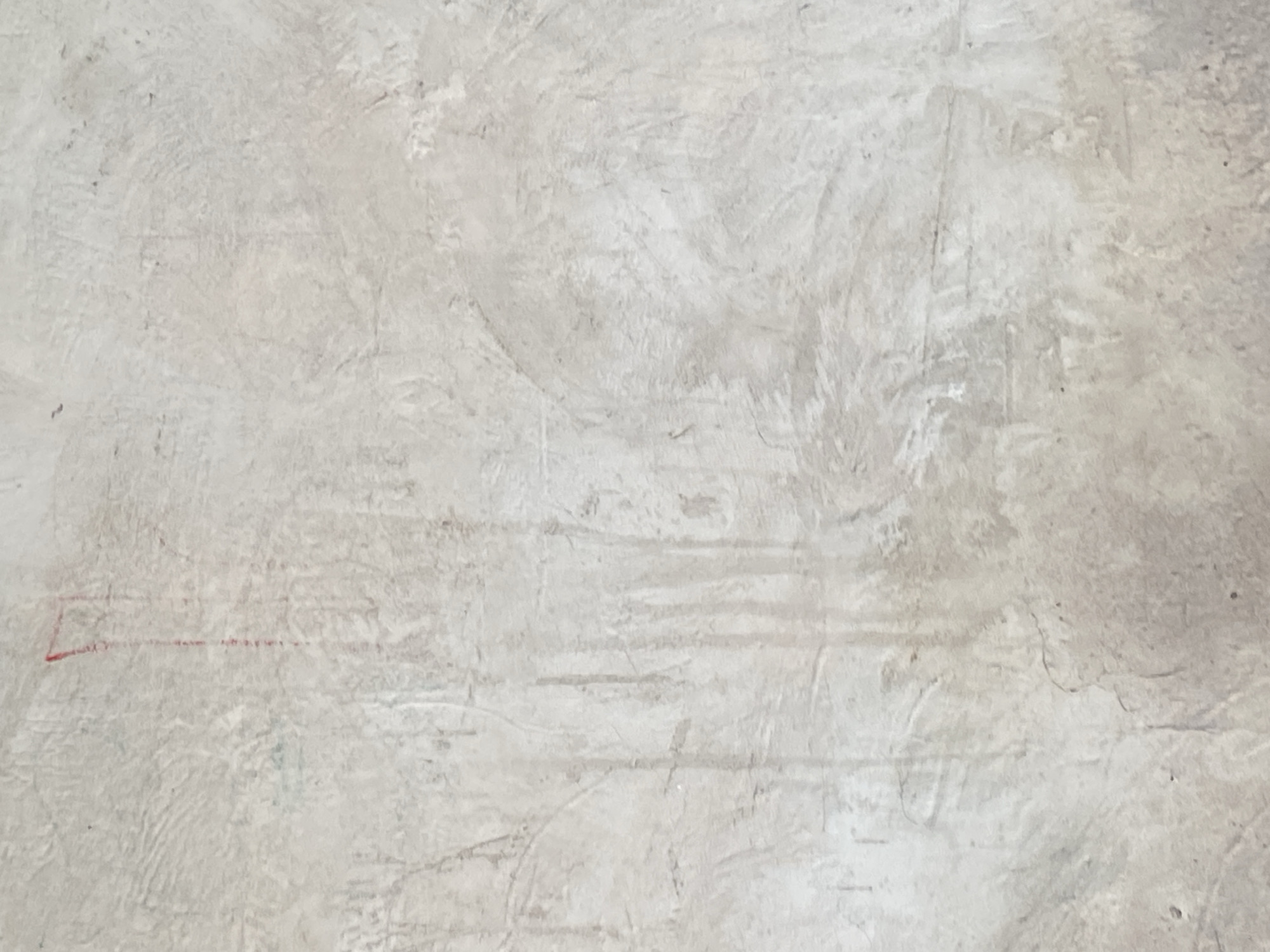 The image displays a close-up, vertically oriented view of a textured, light gray concrete wall. The surface exhibits an uneven, rough texture with visible trowel marks and subtle variations in shading, suggesting it might be an unfinished or weathered surface. A faint vertical streak of red marker is present in the upper left quadrant of the image, extending downwards for a short distance. There are also some faint, darker vertical lines and smudges scattered across the surface, adding to its aged appearance. The lighting is diffused, creating soft shadows that highlight the texture of the concrete. There are no people, animals, or other identifiable objects in the frame. The environment is solely defined by the concrete wall.