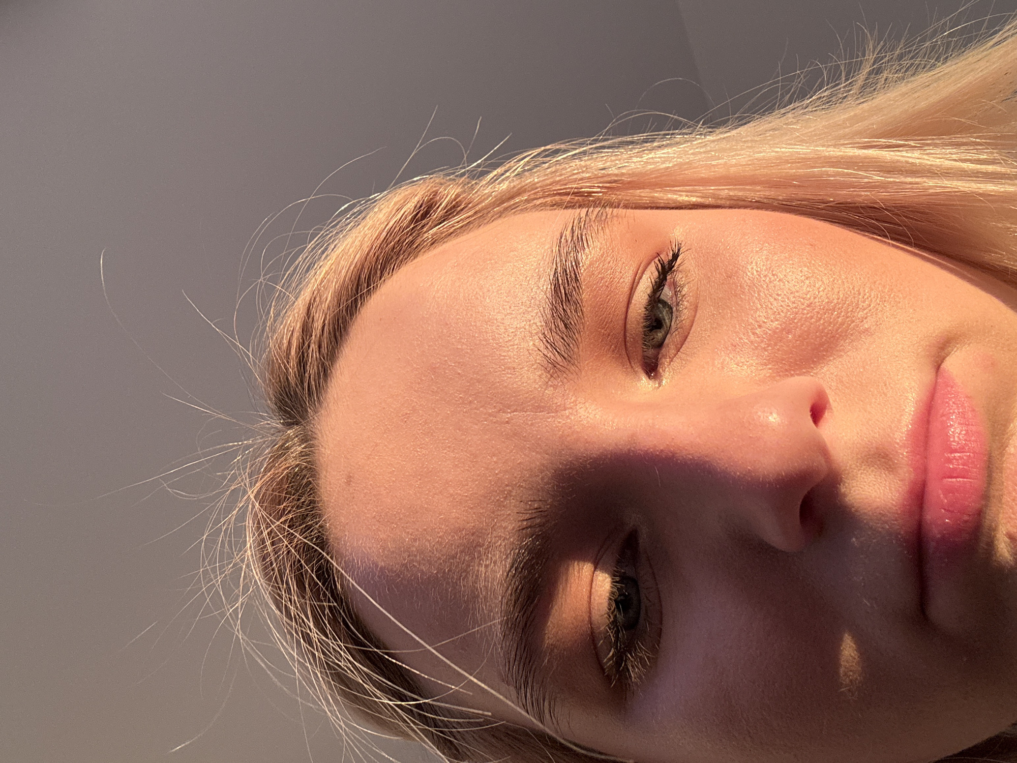 A close-up, angled shot of a person's face with fair skin and blonde hair. The person is looking downwards, with the camera positioned below. Parts of the face are shadowed. The background is a neutral gray. There is no indication of the location being in Vsevolozhsk, Russia.