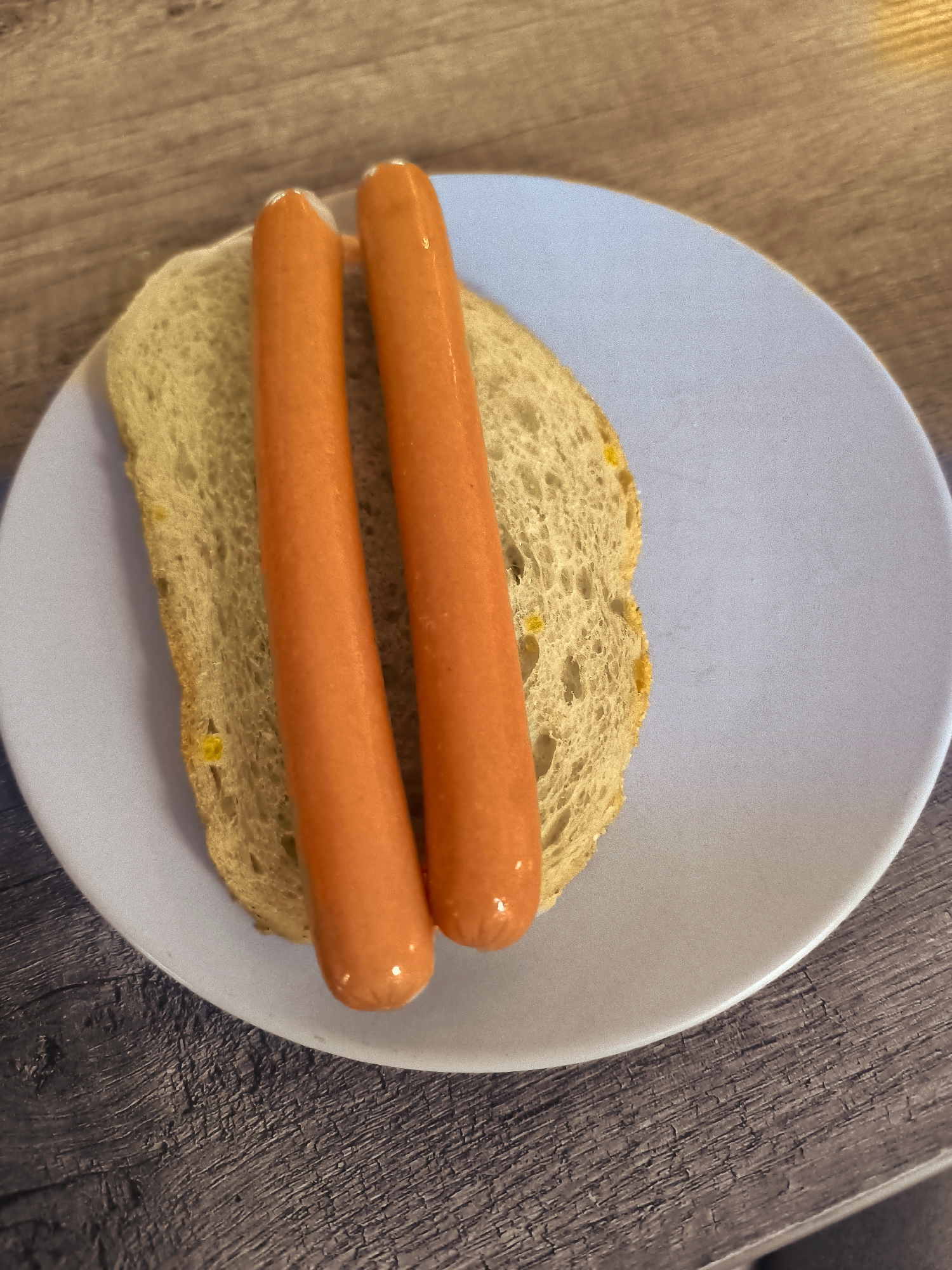 The image shows two hot dogs on a slice of bread placed on a light blue plate. The plate is situated on a dark wooden surface. The background is out of focus, showing more of the wooden surface and suggesting an indoor setting. No people are visible, and no specific location in Almere, Netherlands can be identified.