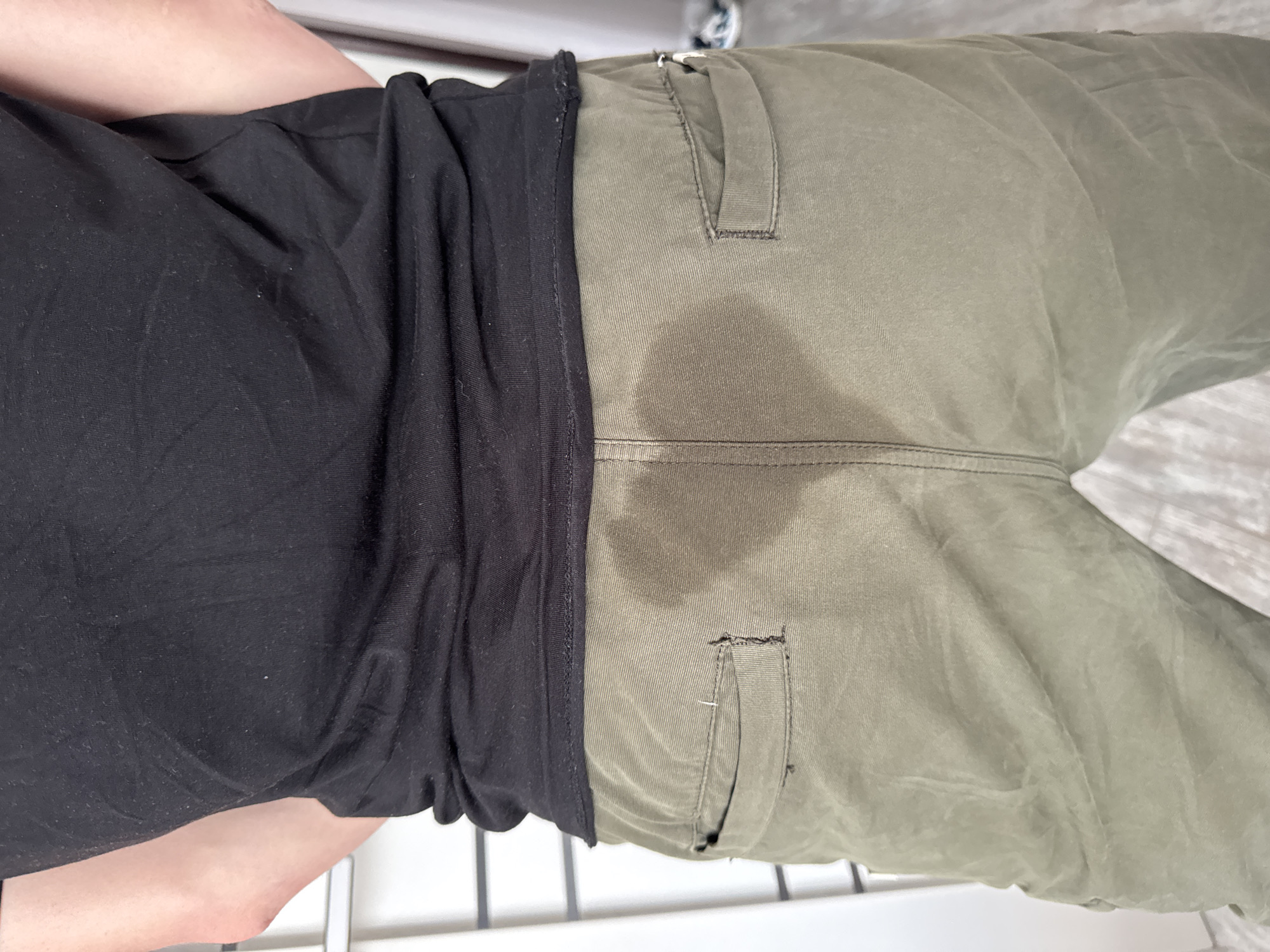 A person wearing a black t-shirt and green pants with a wet spot in the crotch area stands indoors. The location is not discernible from the provided image, and there is no indication of Krasnodar, Russia.