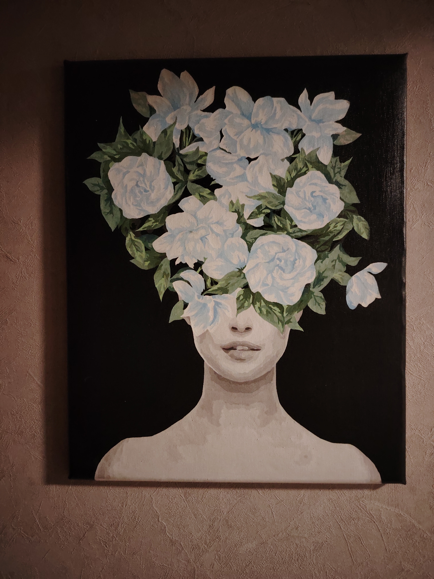The image is a close-up shot of a framed painting hanging on a textured wall. The painting depicts a woman's head and shoulders, but her face is obscured by a dense arrangement of white and light blue flowers with green leaves. The woman's skin is rendered in grayscale tones. The background of the painting is solid black. The wall behind the painting is a light brown color with a textured finish. The image shows only the painting and the wall, and there are no visible people, actions, or interactions. No specific location can be determined from the image, as the wall texture is generic. Марковский is irrelevant.