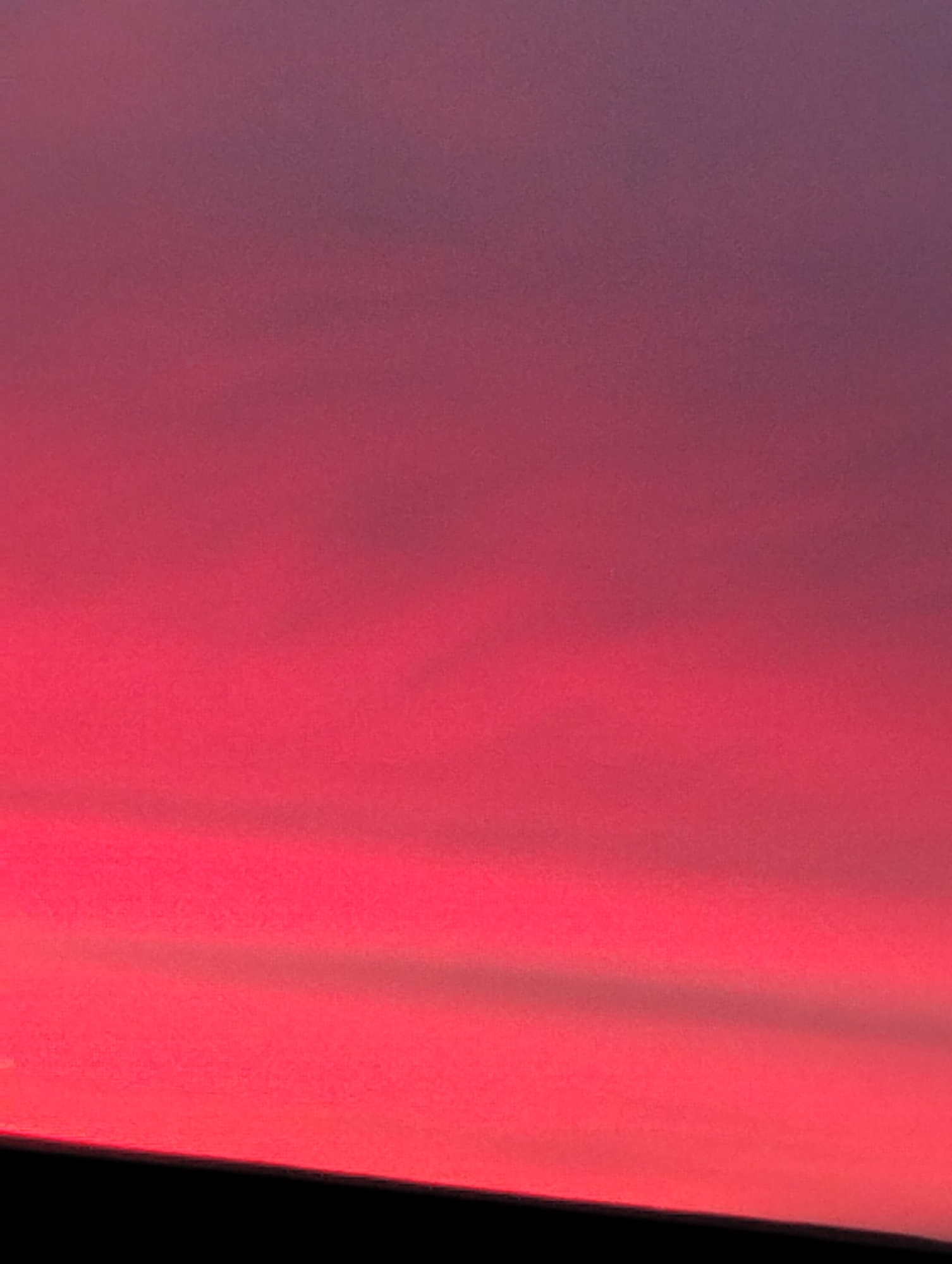 The image depicts a gradient sky transitioning from a deep, almost black color at the bottom, likely the horizon or foreground object obscuring the view, to a vibrant, saturated red-pink in the lower middle section, and gradually fading to a softer, muted purple-pink at the top. The texture is smooth and indistinct, suggesting either atmospheric haze or focus blur. No people, distinct subjects, or objects are directly identifiable, and no actions or interactions are visible. While the description includes the location of Krasnogorskoye, Russia, there is no evident element in the image that confirms it, or provides direct information related to it.