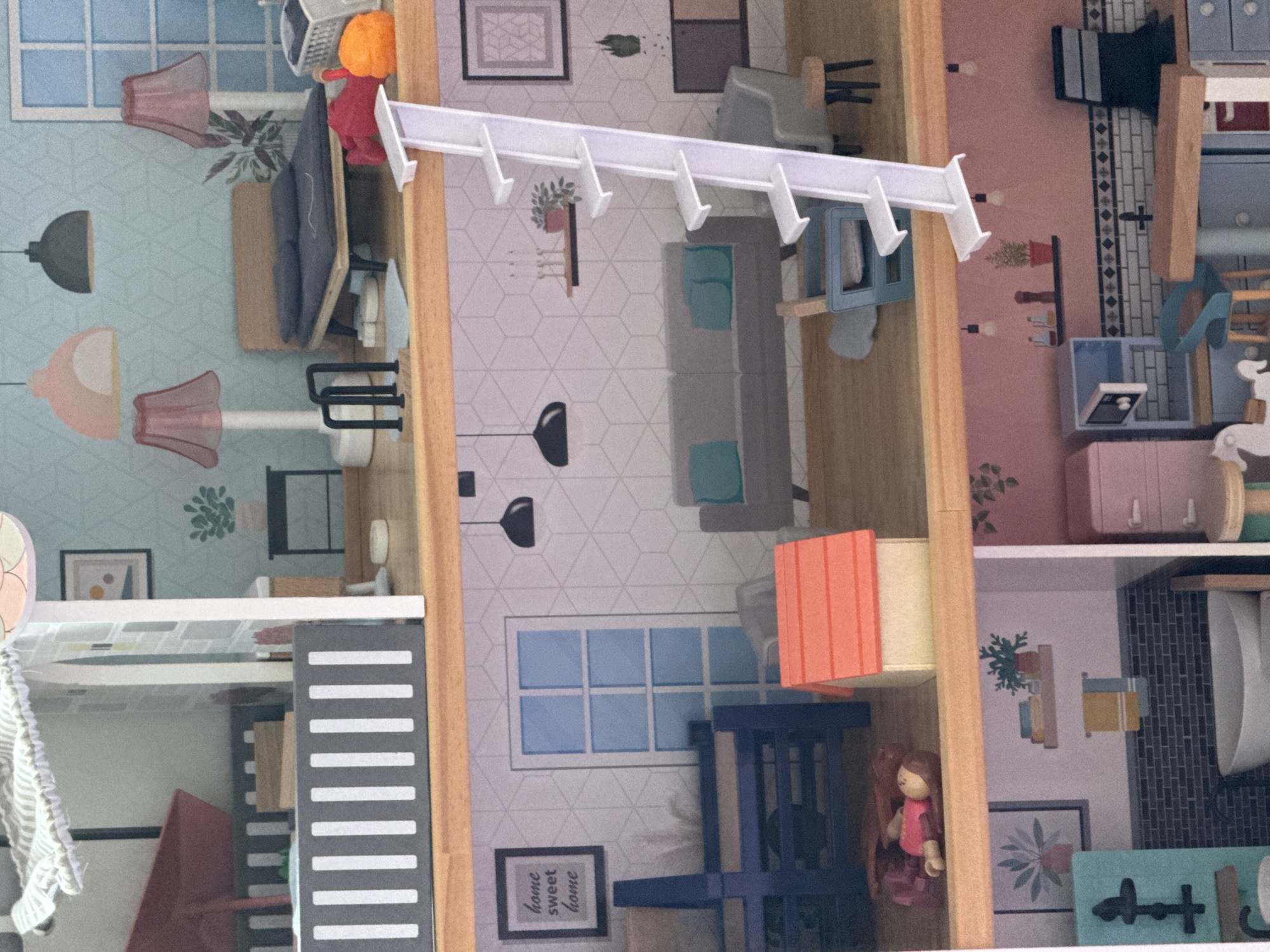 A miniature dollhouse is depicted, containing multiple rooms with furnishings and decorations. The rooms feature various color schemes and wallpaper patterns. Specific items visible include furniture, plants, windows, artwork, and a doll. The dollhouse is not located in Sofia, Bulgaria.