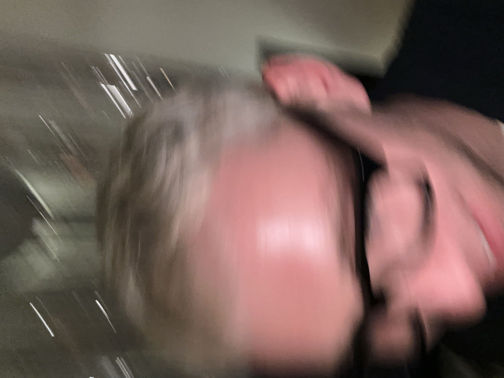 The image is blurry and indistinct, but appears to show a person's head and upper body. The person has gray hair and their skin appears reddish. The background is dark and out of focus, with some lighter shapes possibly indicating a wall or other structure. It is impossible to determine the location in London or any specific details about actions or interactions from this image.