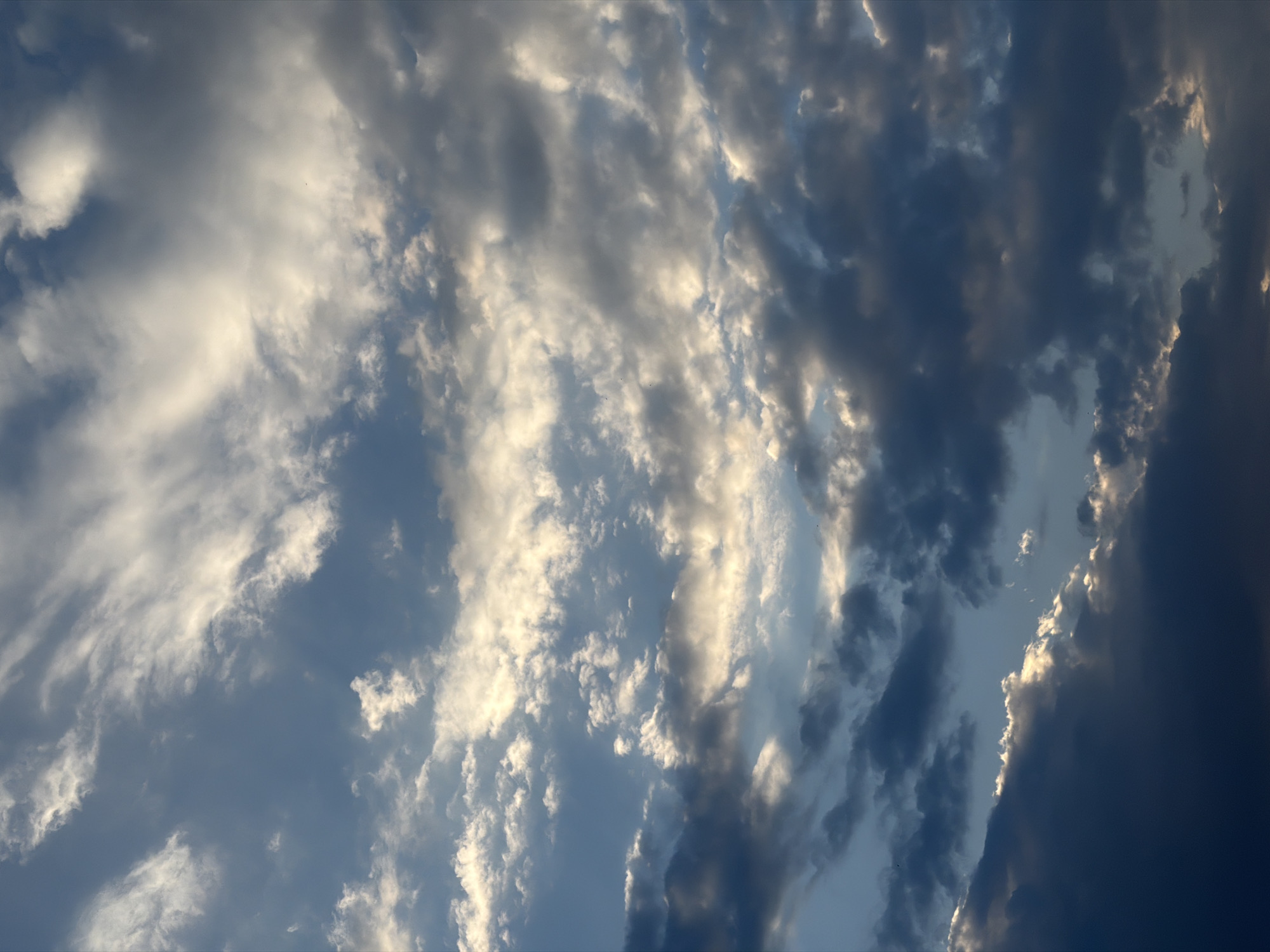 The image displays a dramatic sky filled with a mix of dark, heavy clouds and bright, illuminated clouds, suggesting an impending storm or the aftermath of one. The clouds are textured and layered, with sunlight breaking through in some areas, creating a contrast between light and shadow. The overall impression is one of natural beauty and the power of the elements. There are no identifiable landmarks or structures that would suggest a specific city or location. The scene is devoid of any human presence or activity.