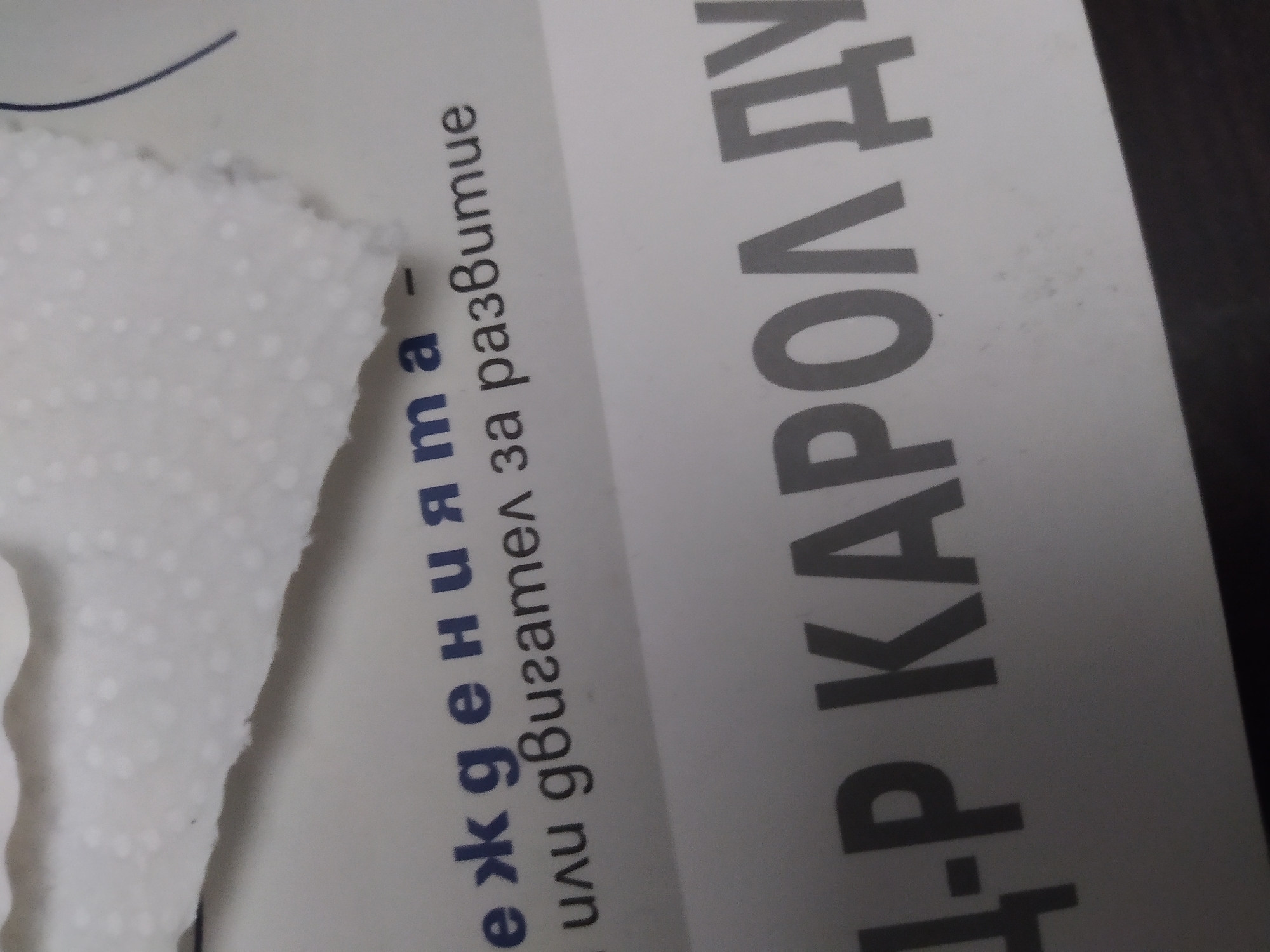 The image shows a close-up of a piece of textured white material, possibly a tissue or paper towel, partially covering text printed on a white surface. The text is in Cyrillic script, with the phrase "еждеенията или двигател за развитие" and "Д-р Карол Ду" visible. The text appears to be part of a book or poster. The location is likely Sofia, Bulgaria, due to the Cyrillic text.