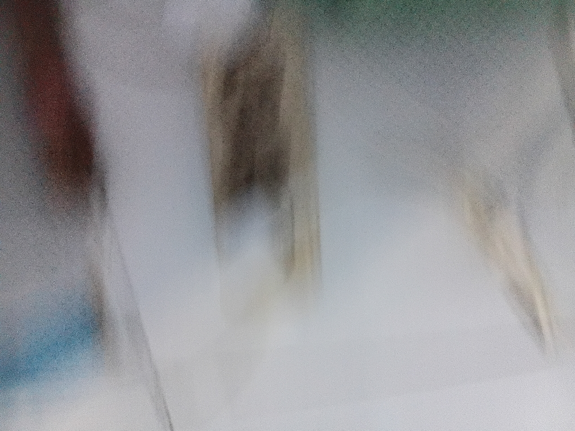 This image depicts a blurred, abstract scene with no discernible people, objects, or specific actions. The background is a gradient of muted colors, primarily grays and whites, with faint hints of tan and blue. The overall impression is one of a low-resolution, out-of-focus photographic capture. There is no information present in the image that would allow for an identification of its location within Tanggul Wetan, Indonesia, or any other specific geographical context.