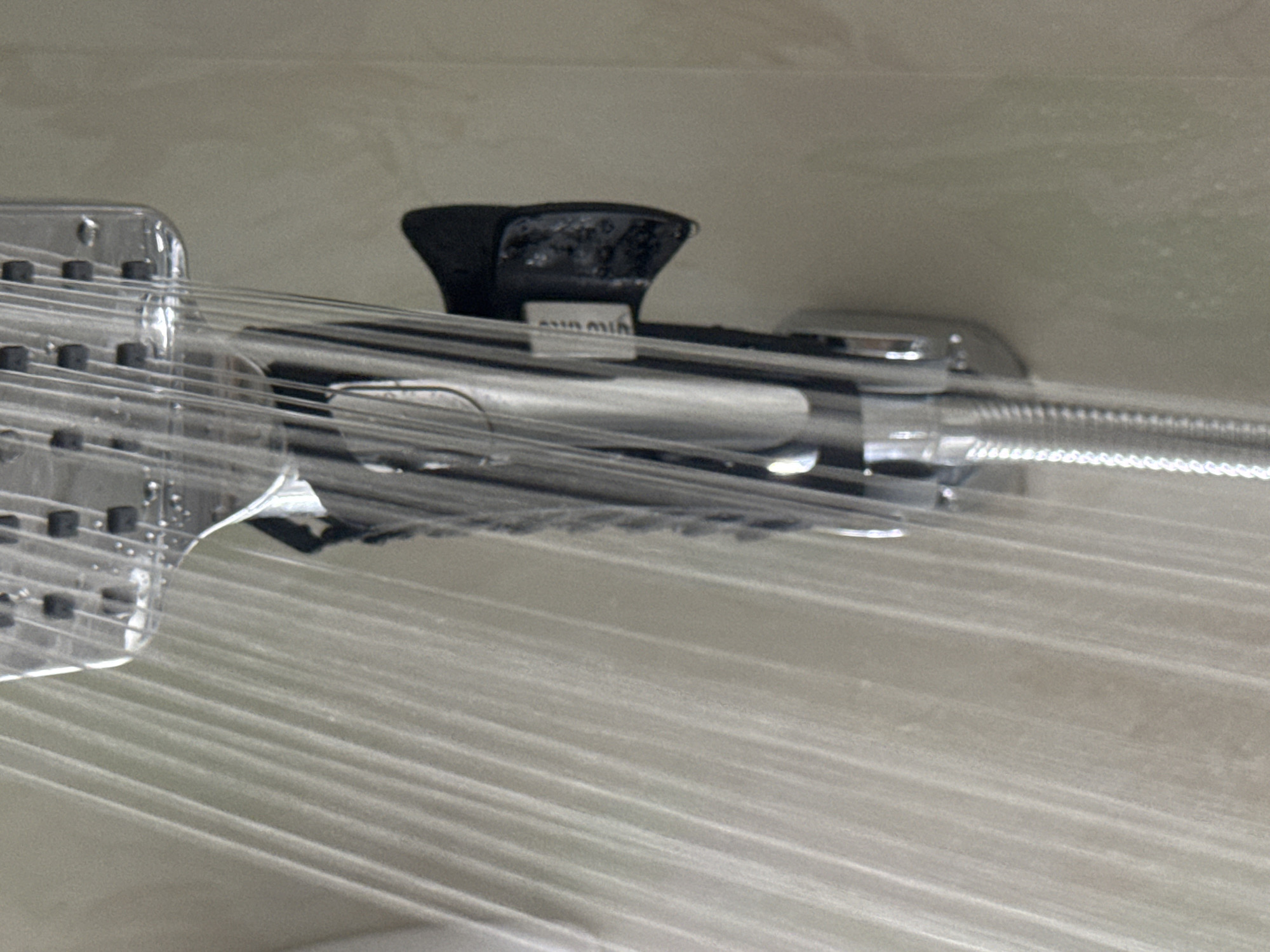 A close-up, indoor, eye-level shot captures a shower head with water spraying from it. The shower head is made of chrome and has a black handle. The water is spraying in multiple streams and appears to be hitting a tiled wall, which is a pale, neutral color. The background is slightly out of focus, highlighting the shower head and the water spray. There are no people visible in the image. The scene takes place in a shower, likely in a bathroom. The location in Saratov, Russia cannot be determined from the image alone.