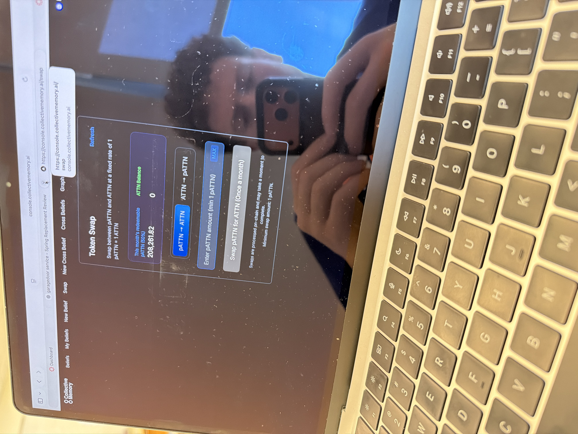 The image shows a person using a laptop. The laptop screen displays the console of "collectivememory.ai" at "https://console.collectivememory.ai/swap," specifically the "Token Swap" interface. The interface allows swapping between PATTN and ATTN tokens at a fixed rate of 1 PATTN = 1 ATTN. The month's redeemable PATTN is 208,261.82. The user has the option to swap PATTN to ATTN or ATTN to PATTN. The screen indicates a field to enter the pATTN amount with a minimum of 1 pATTN. A "MAX" button is present. The laptop keyboard is visible.
The image does not provide information to suggest the location is New York City or anywhere else in the United States.