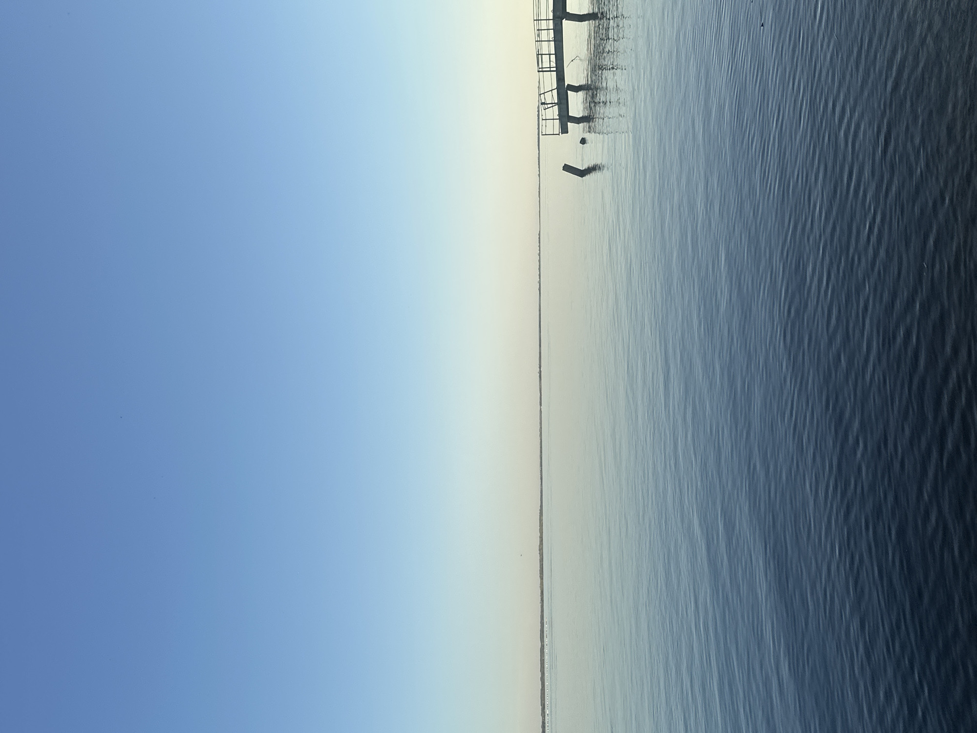 The image shows a body of water under a clear blue sky. A structure resembling a pier is visible on the right side, partially extending into the water. The water's surface shows subtle ripples. The location is likely near Soroch'i Gory, Russia, based on the likely origin of the image. There are no people visible in the scene.