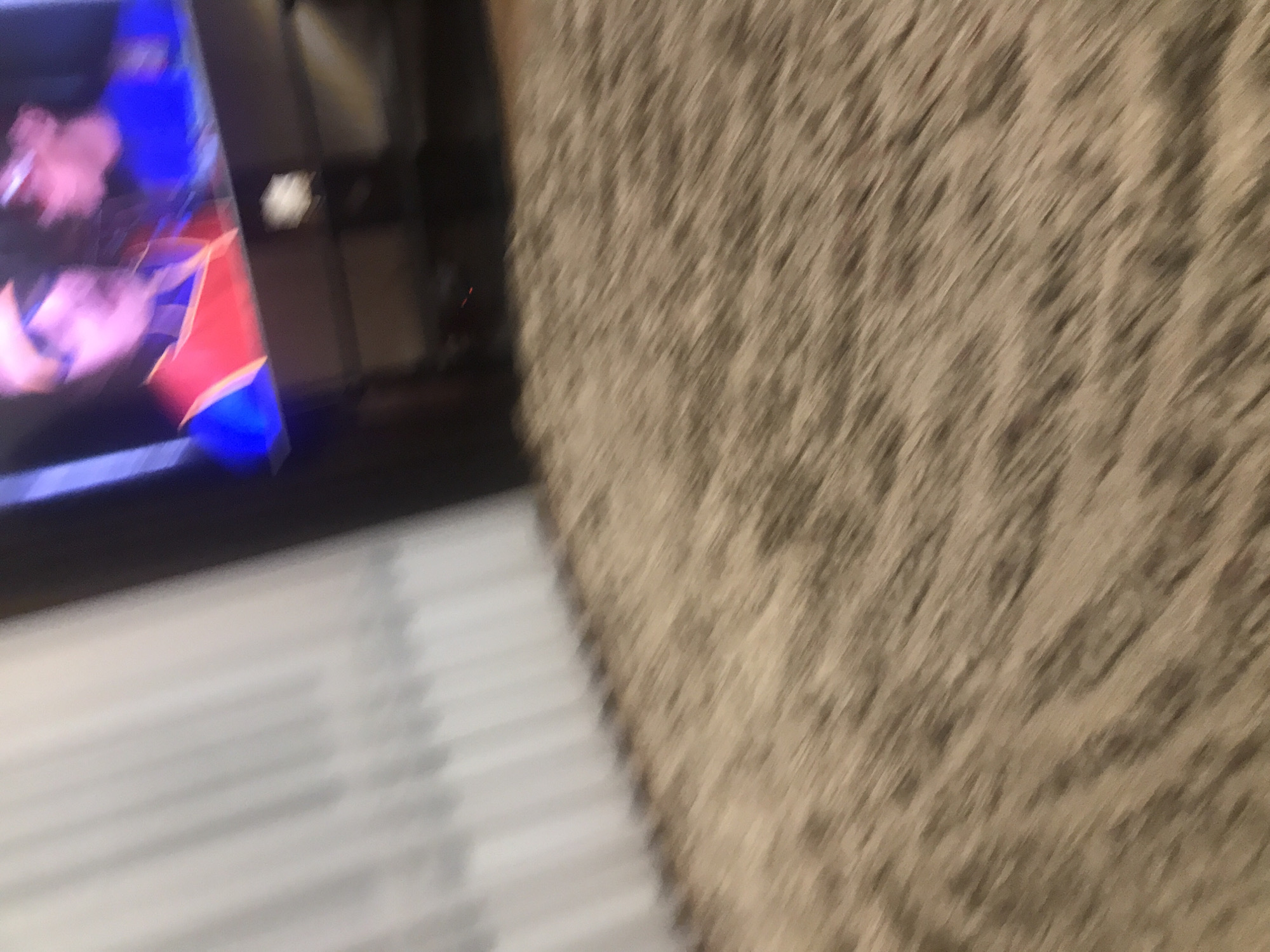 A blurry image depicts a television screen displaying an indeterminate colorful image. The TV is positioned near a wall covered in a textured beige material. Below the television screen, horizontal lines suggest a surface like a floor or a table. The location in Yerevan, Armenia, is not discernible from the provided image.