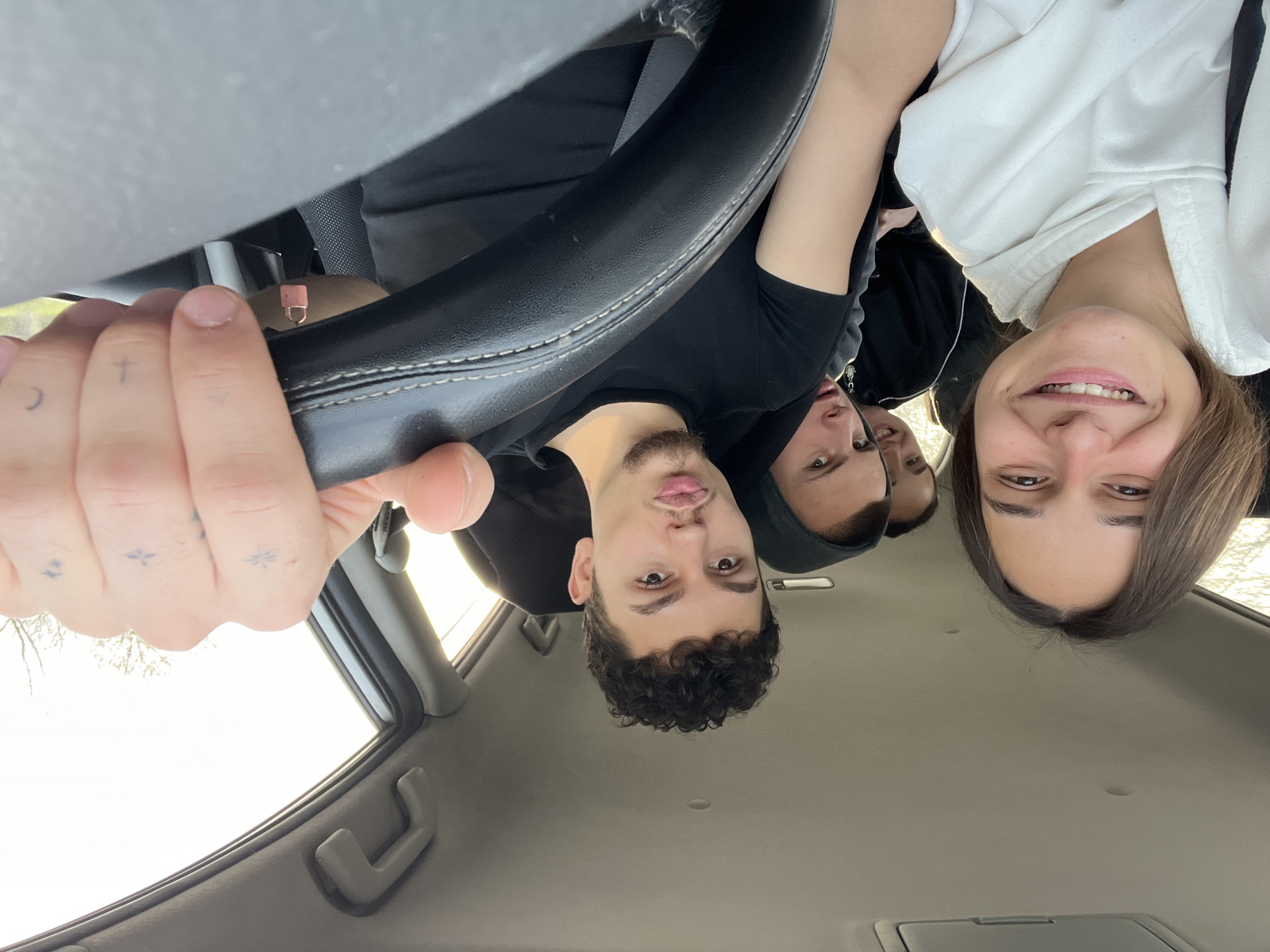 Four young people are in the interior of a car. One person is holding the steering wheel. One person is wearing a white hoodie. The setting may be Novakovo, Bulgaria.