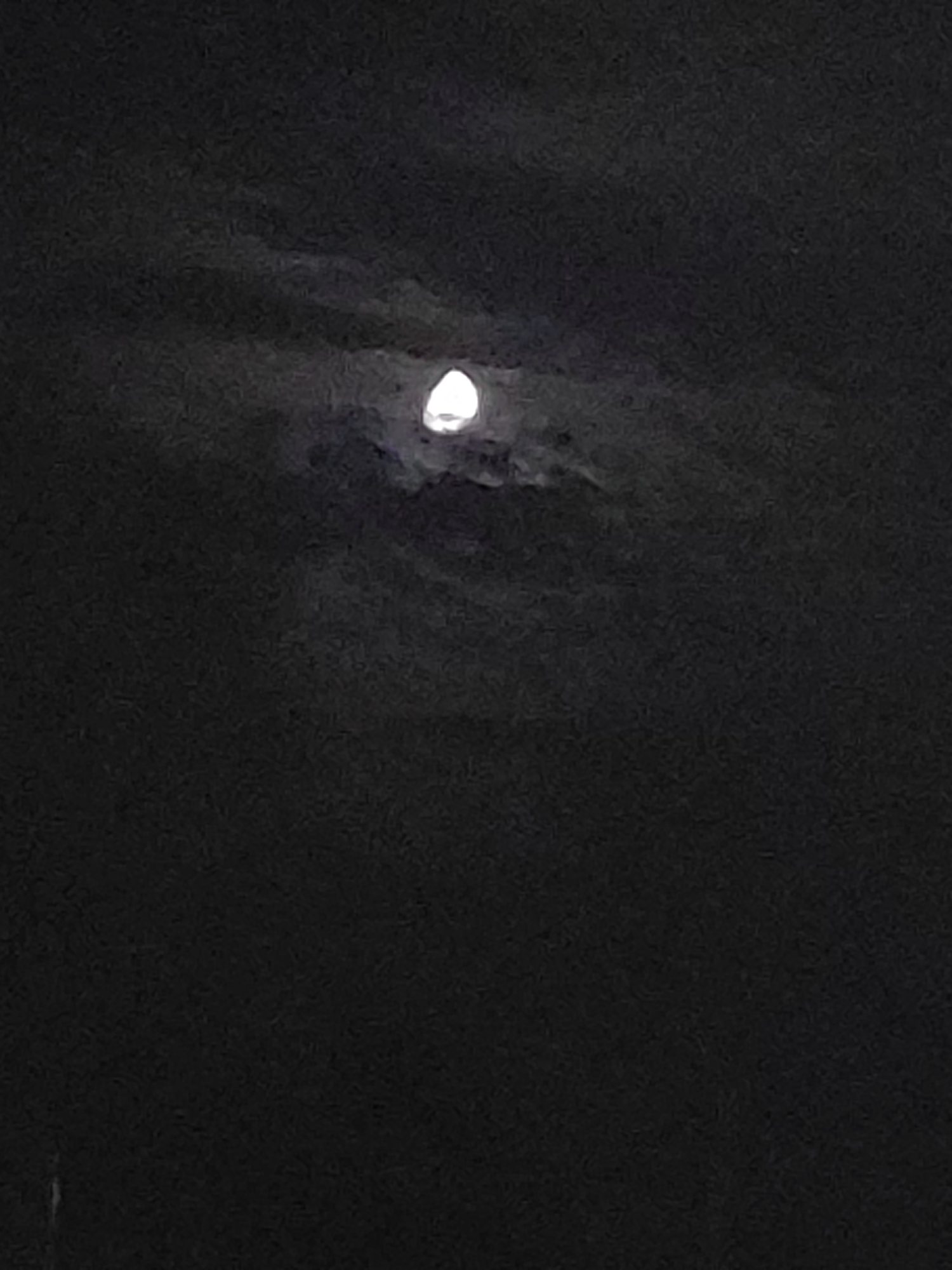 A full moon is visible in a dark, cloudy sky. The moon is bright and luminous, partially obscured by wispy clouds. The surrounding sky is predominantly black, suggesting nighttime. There is no indication of a specific location within Villarejo de Fuentes, Spain. The image lacks any discernible subjects, objects, or actions.