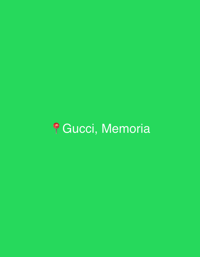 The image features a solid, vibrant green background devoid of any discernible scenery or objects other than digital elements. Centered horizontally and slightly above the vertical midpoint, a red map pin emoji (📌) is displayed. To the right of the map pin, the text "Gucci, Memoria" is visible in a light, sans-serif font.
There are no people or specific activities taking place within the static image. The bright green color fills the entire frame, giving the impression of a digital interface or a graphic design. The map pin emoji combined with the text "Gucci, Memoria" strongly suggests a location tag or a reference to a specific entity. Given the location context of Milan, Italy, a global fashion capital and home to numerous luxury brands, it is highly probable that "Gucci, Memoria" refers to the Italian luxury fashion house, possibly indicating a store location, an event related to the brand, or even its unisex fragrance "Gucci Memoria d'un Odore" (also known as Gucci Memoria). The simplicity of the image, with its single color background and minimal text, focuses attention directly on the brand name and the accompanying term "Memoria," which means "memory" in Italian.