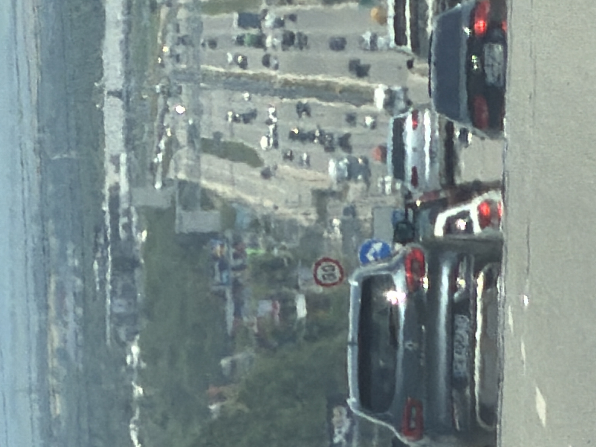 The image captures a highway scene, likely in or near Sofia, Bulgaria. In the foreground, a dark-colored car is visible from behind, with its license plate partially obscured by glare. To the right, another dark-colored car is also seen from the rear. In the middle ground, a lighter-colored car is positioned. Further down the highway, numerous vehicles are in motion or stopped in traffic. Beyond the highway, a hillside covered with greenery and buildings suggests an urban or semi-urban environment. A circular speed limit sign with "60" is visible on the side of the road. The overall lighting and atmospheric conditions indicate it is daytime, with a hazy sky.
