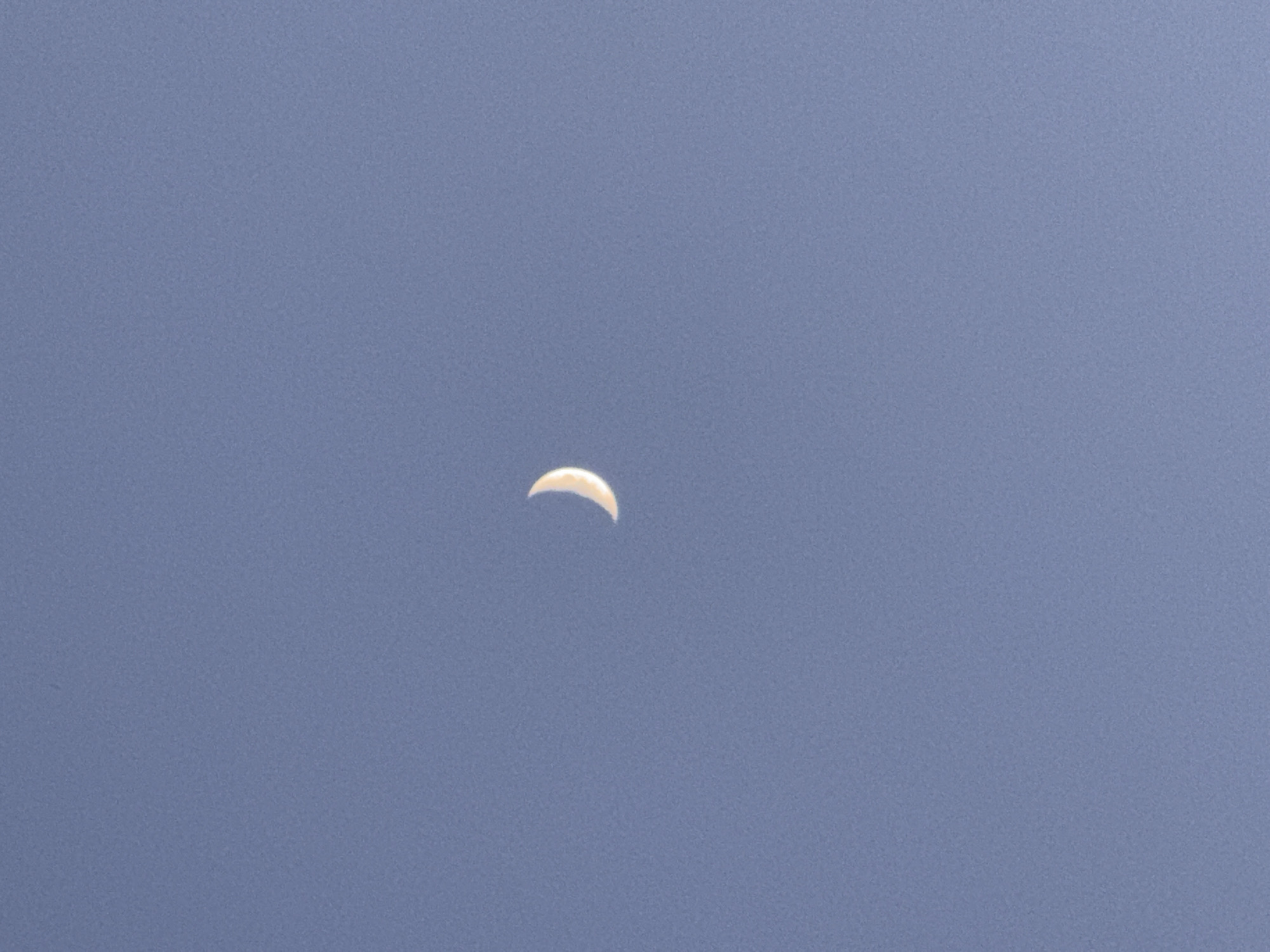 A crescent moon is visible in a clear, pale blue sky. The moon is illuminated from the right, with its lit portion forming a thin arc. The sky is a uniform color with no other celestial bodies or atmospheric phenomena visible. No terrestrial features or geographical markers are present in the image, thus the location in Burgas, Bulgaria, cannot be determined.