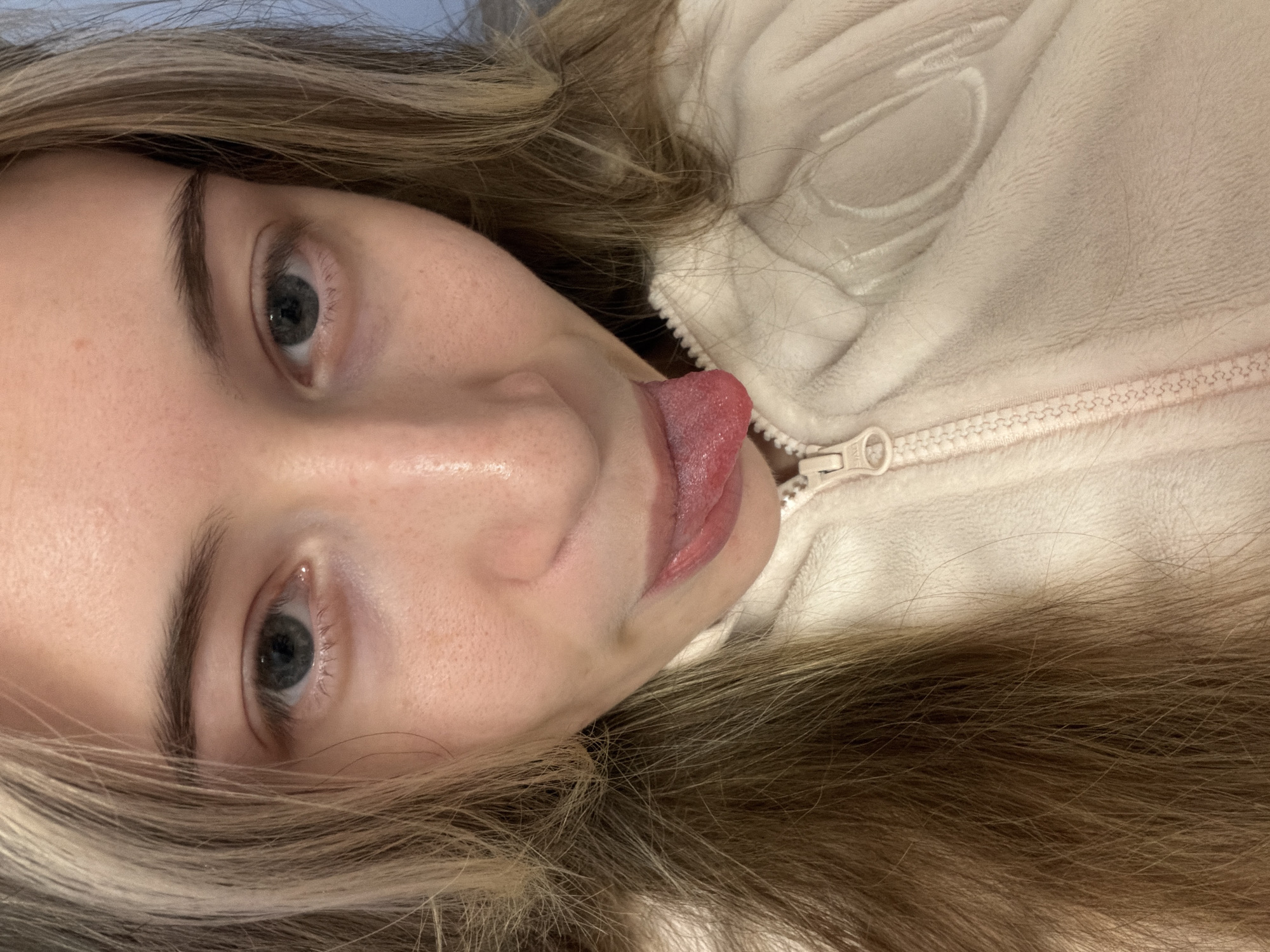 A close-up, selfie-style image shows a young Caucasian woman with blonde and brown hair sticking her tongue out. Her eyes are gray. She is wearing a light-colored, zippered fleece jacket. The image does not provide any information about the location in Plovdiv, Bulgaria.