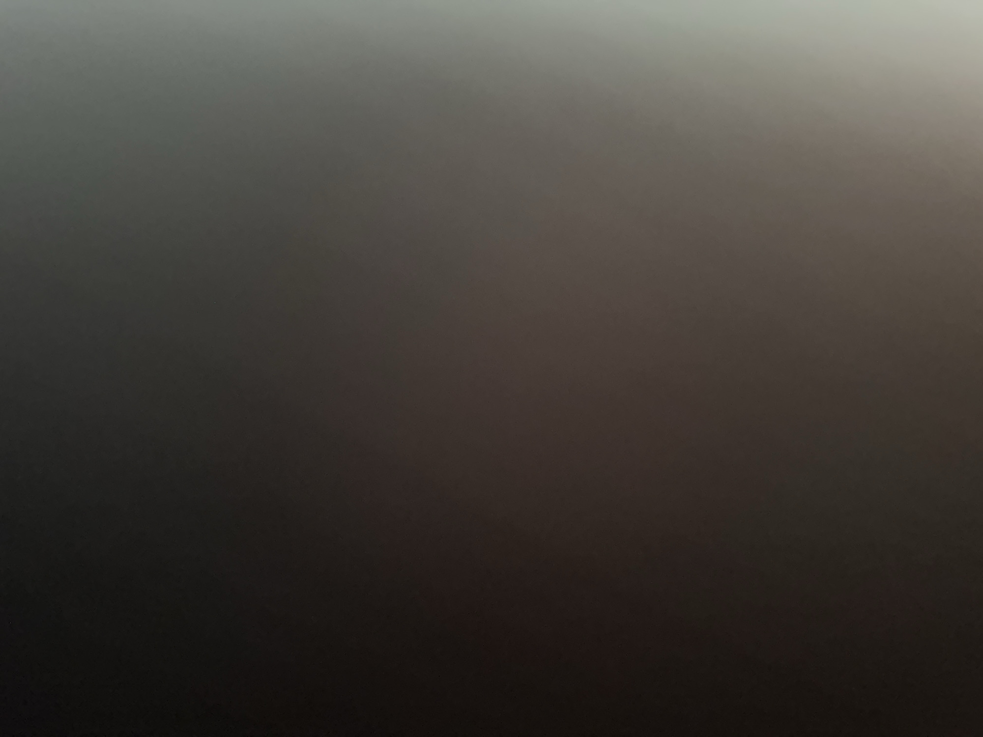 The image is a blurry, abstract, and dark composition with a gradient of grays and blacks, fading to a lighter gray or white at the top. There are no discernible subjects, objects, scenes, or settings. No activity or event is taking place. There are no notable details such as time of day, weather, location cues, or emotions. No text is visible. The image appears to be a visual abstraction rather than a representation of a concrete subject.