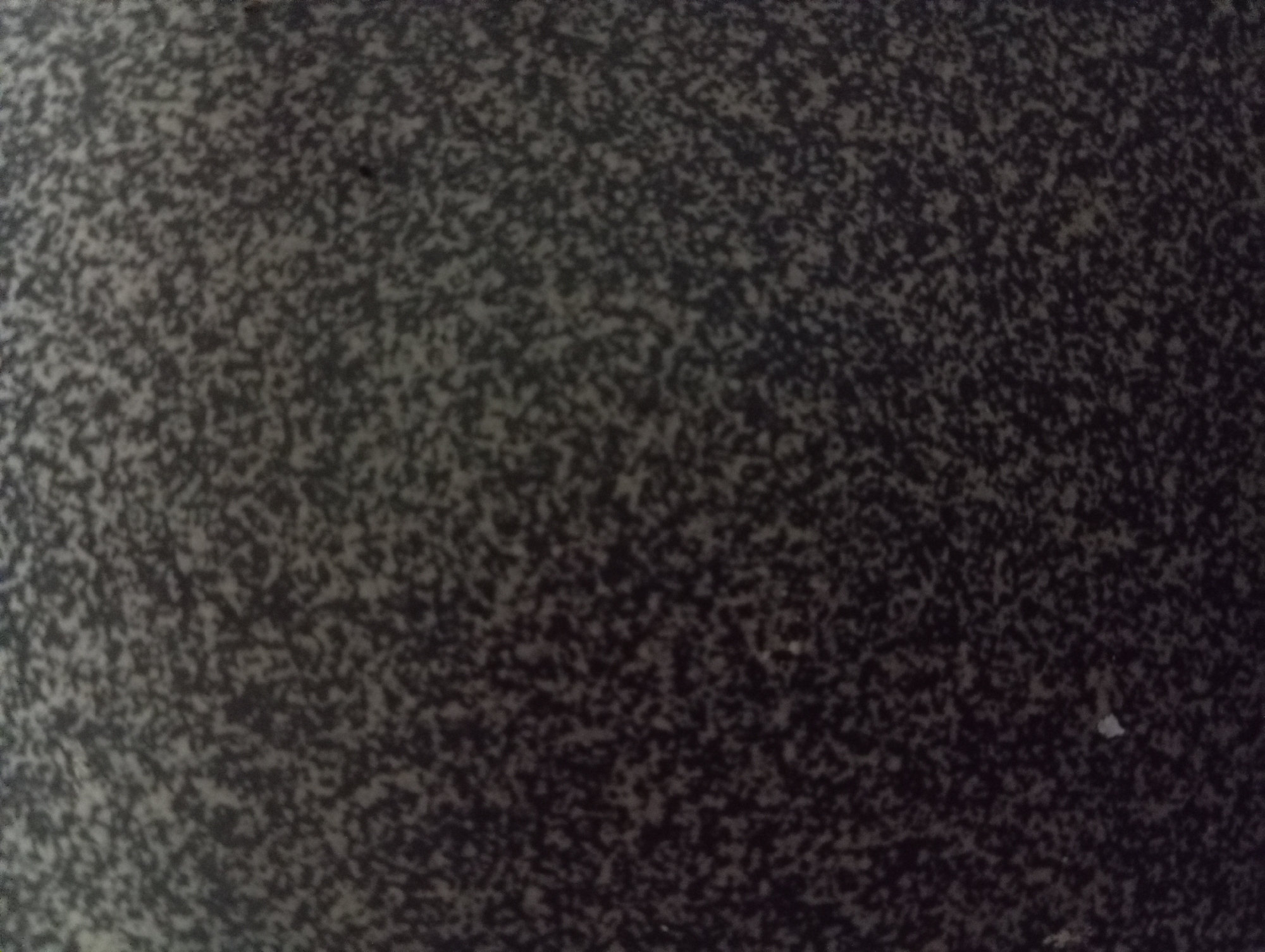 The image shows a close-up, abstract view of a speckled surface, possibly granite or a similar material, with a dark gray background and irregular, lighter gray and black speckles. There are no discernible people, objects, or actions. The texture appears granular and uneven. The image does not contain any elements that can be used to identify a specific location within Hlynytsi, Ukraine.